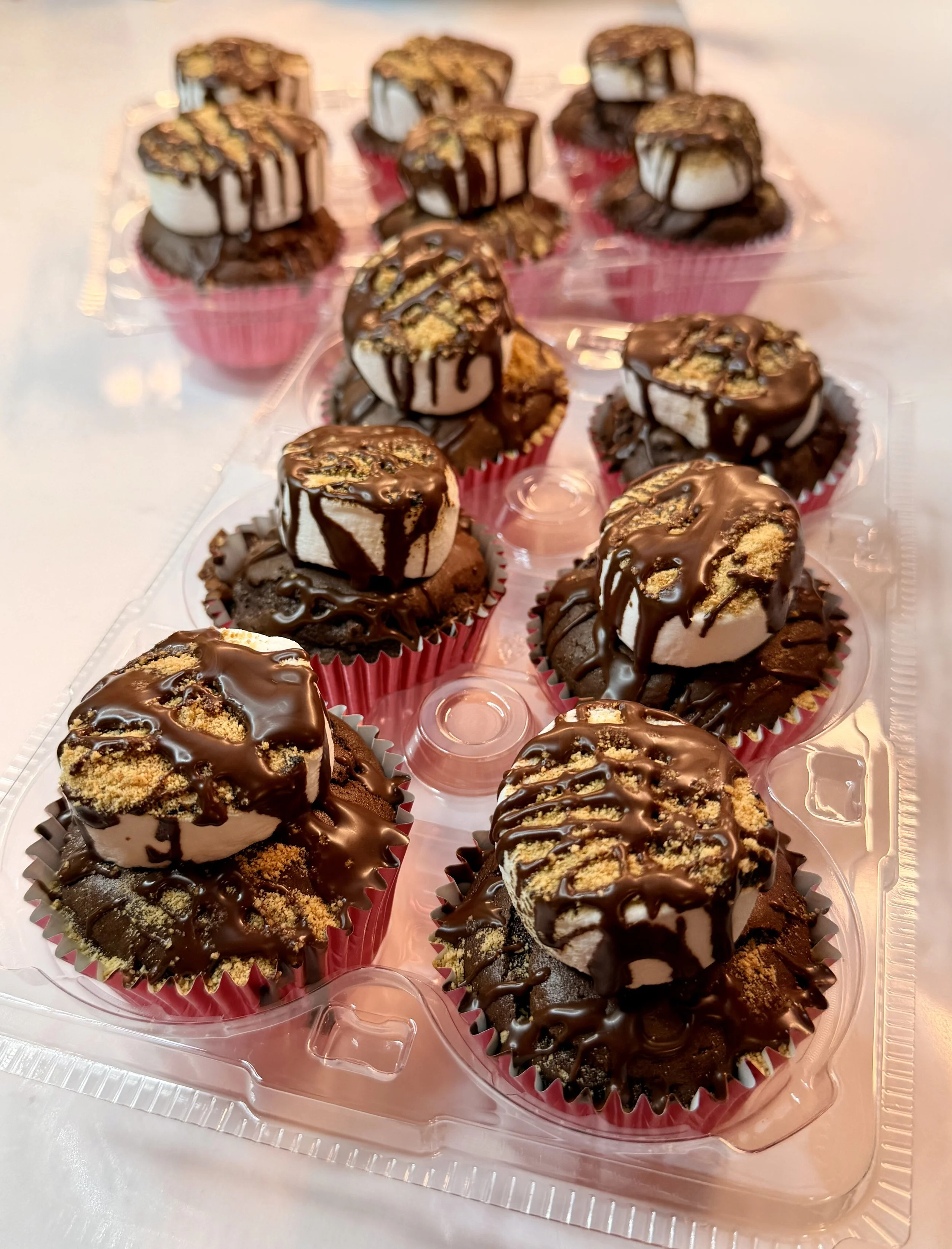 A plastic container with multiple chocolate-covered ice cream sundaes topped with crushed cookies and chocolate drizzle.