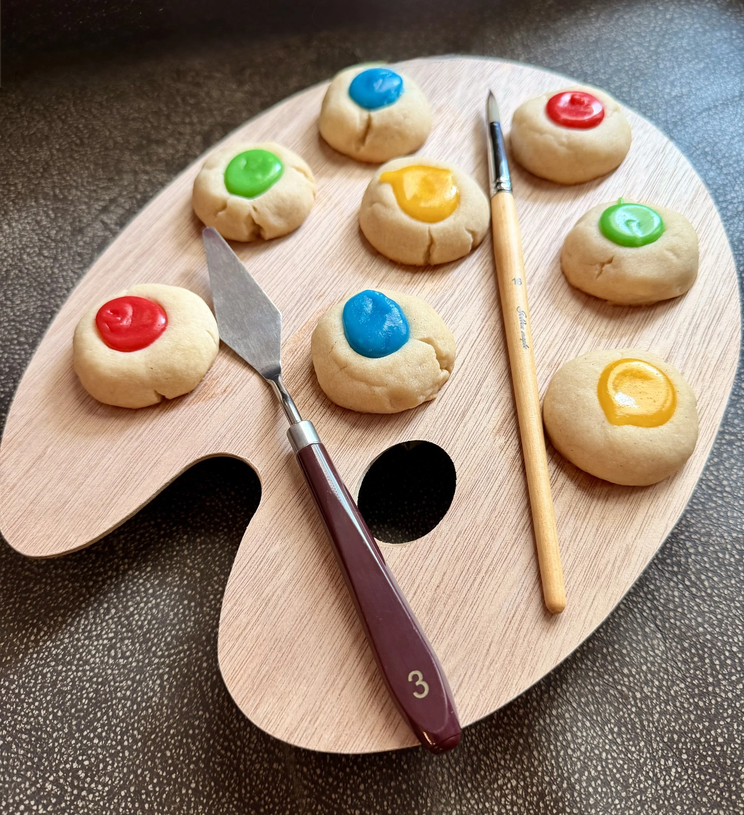 Colorful cookies on a wooden board with a cookie cutter and a number 3 cake decorating tool.