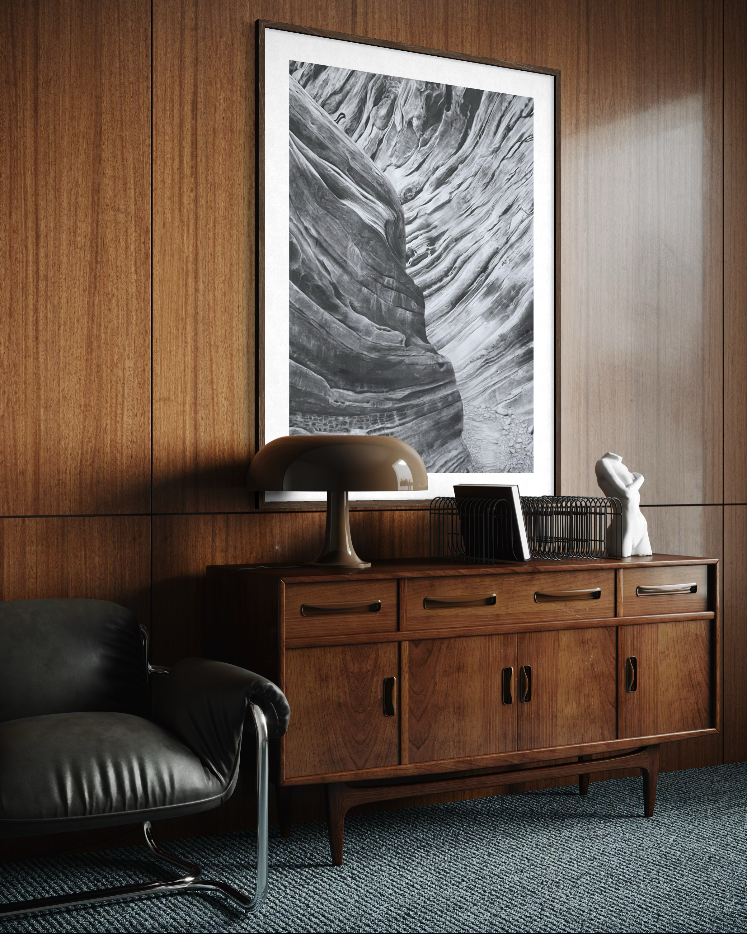 Wood-paneled wall with a large black-and-white abstract artwork, a dark leather chair, a beige table lamp, and decorative items on a wooden sideboard.