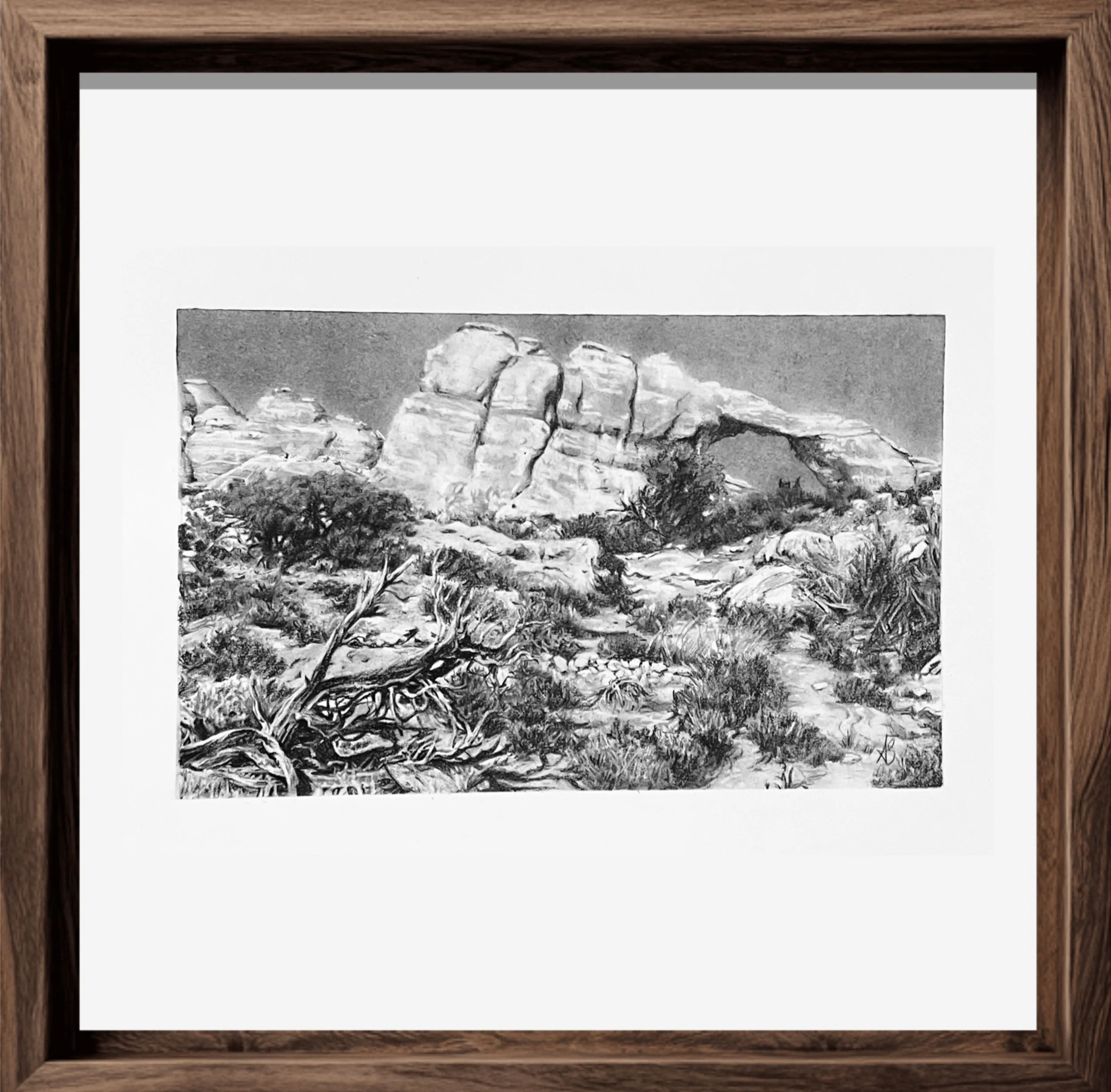 Black and white painting in a wooden frame depicting a landscape with large rocks and mountains in the background.