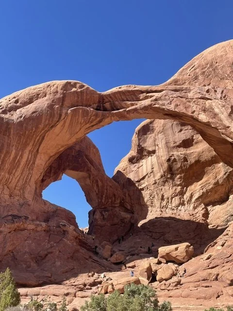 A natural rock formation of two large arches in a desert landscape with clear blue sky.