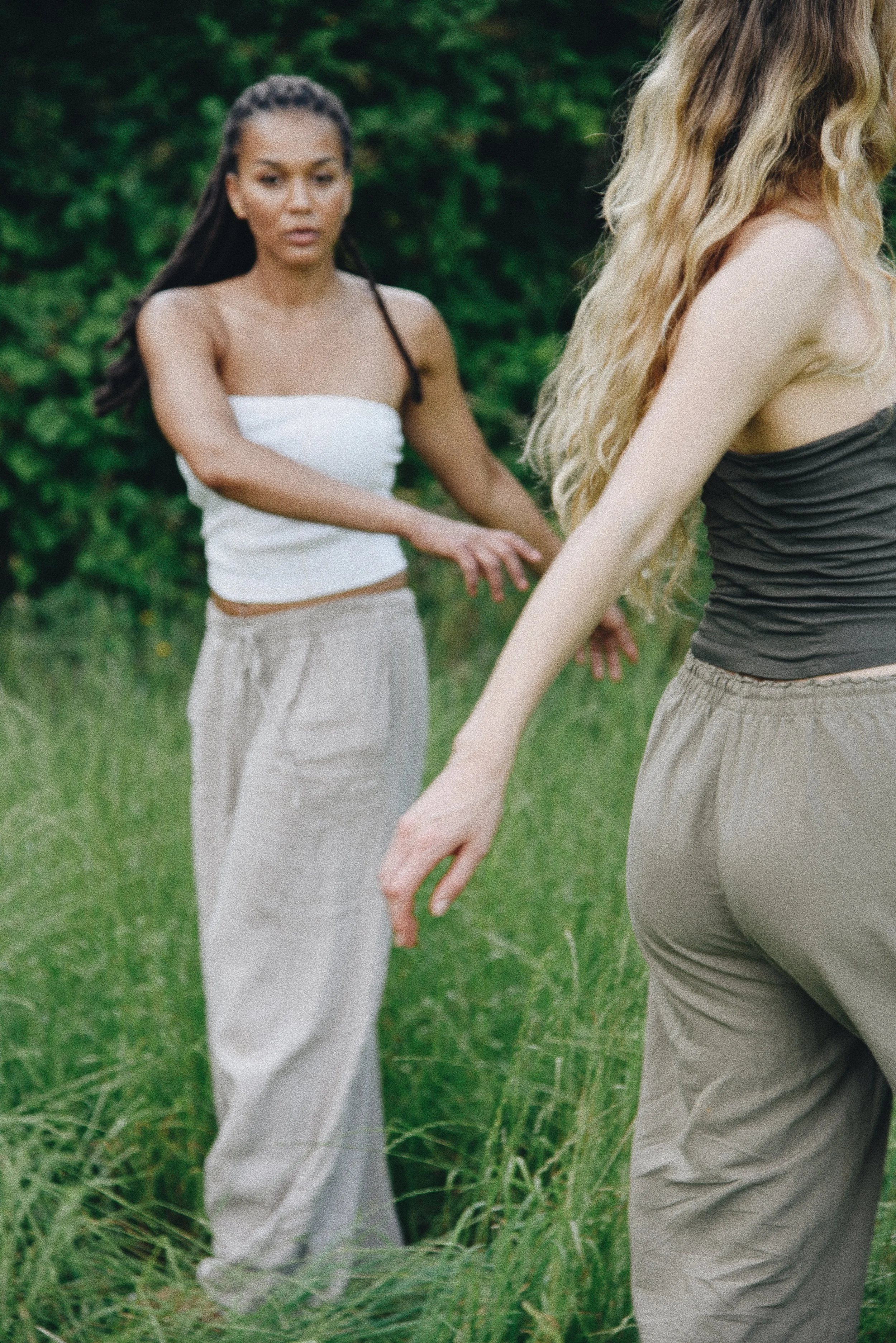 Zwei Frauen im Grünen, die sich gegenseitig an den Händen berühren, während sie in einem Feld stehen.