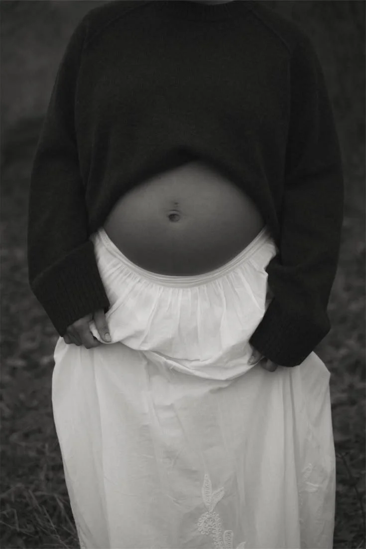 Schwarz-Weiß-Foto eines Menschen mit Blick auf den Bauch, der eine dunkle Jacke und einen weißen Rock trägt.