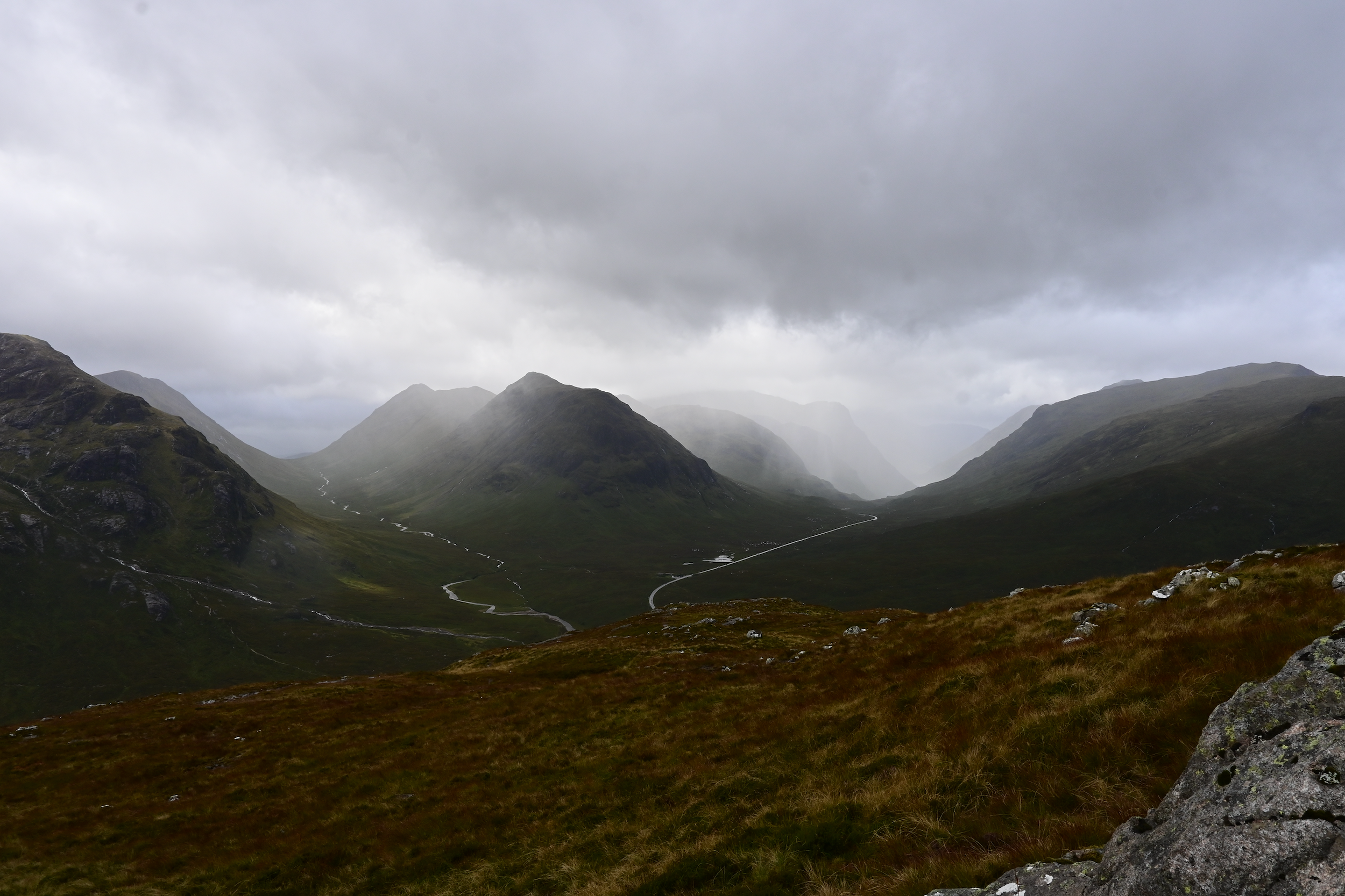 Scenic view of a lush green valley surrounded by mountains under a cloudy sky.