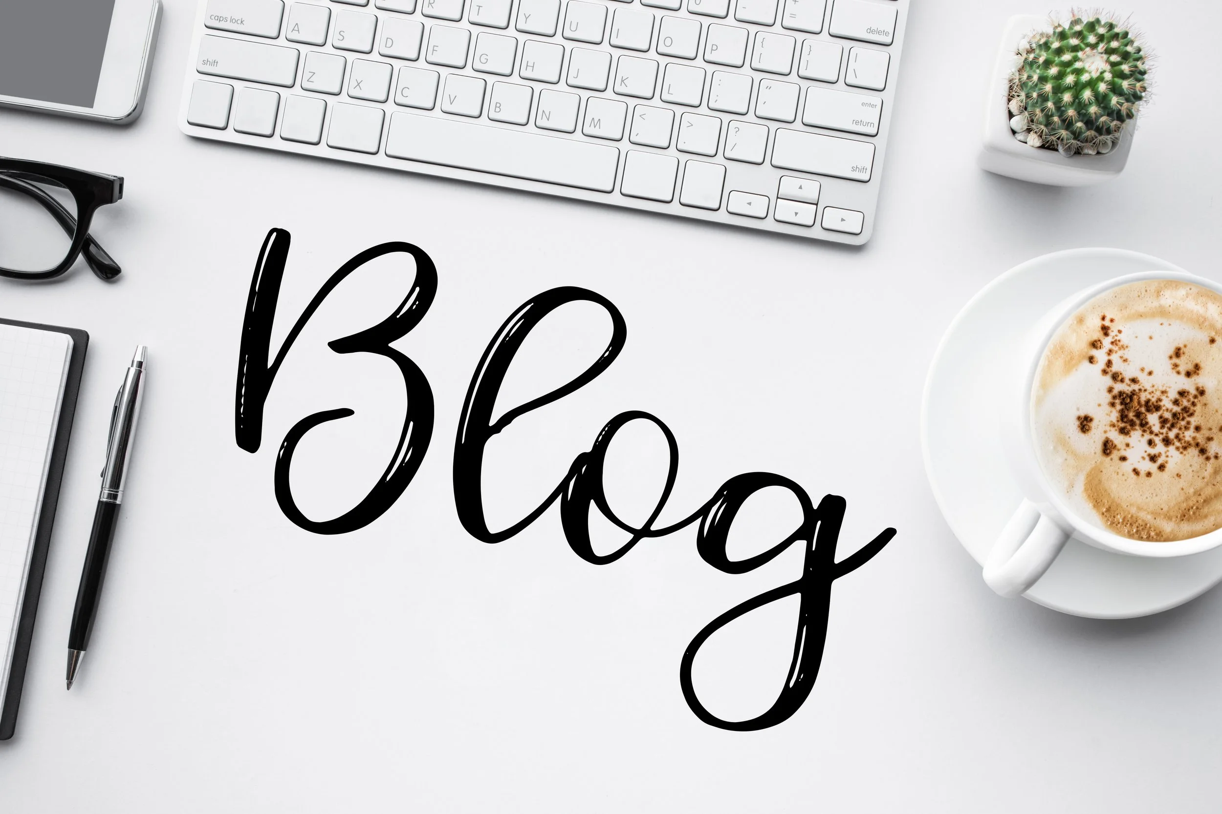 A white workspace with a computer keyboard, a smartphone, a pair of glasses, a notebook with a pen, a cactus in a pot, a cup of coffee, and the words 'Blogging' written in black cursive text.