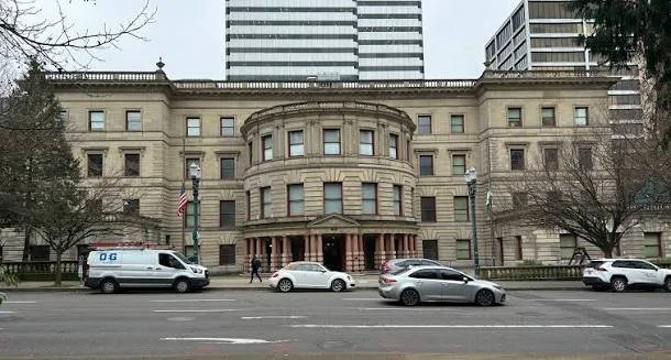 Historic stone building with rounded central section and columns, situated along a city street with parked cars and pedestrians.