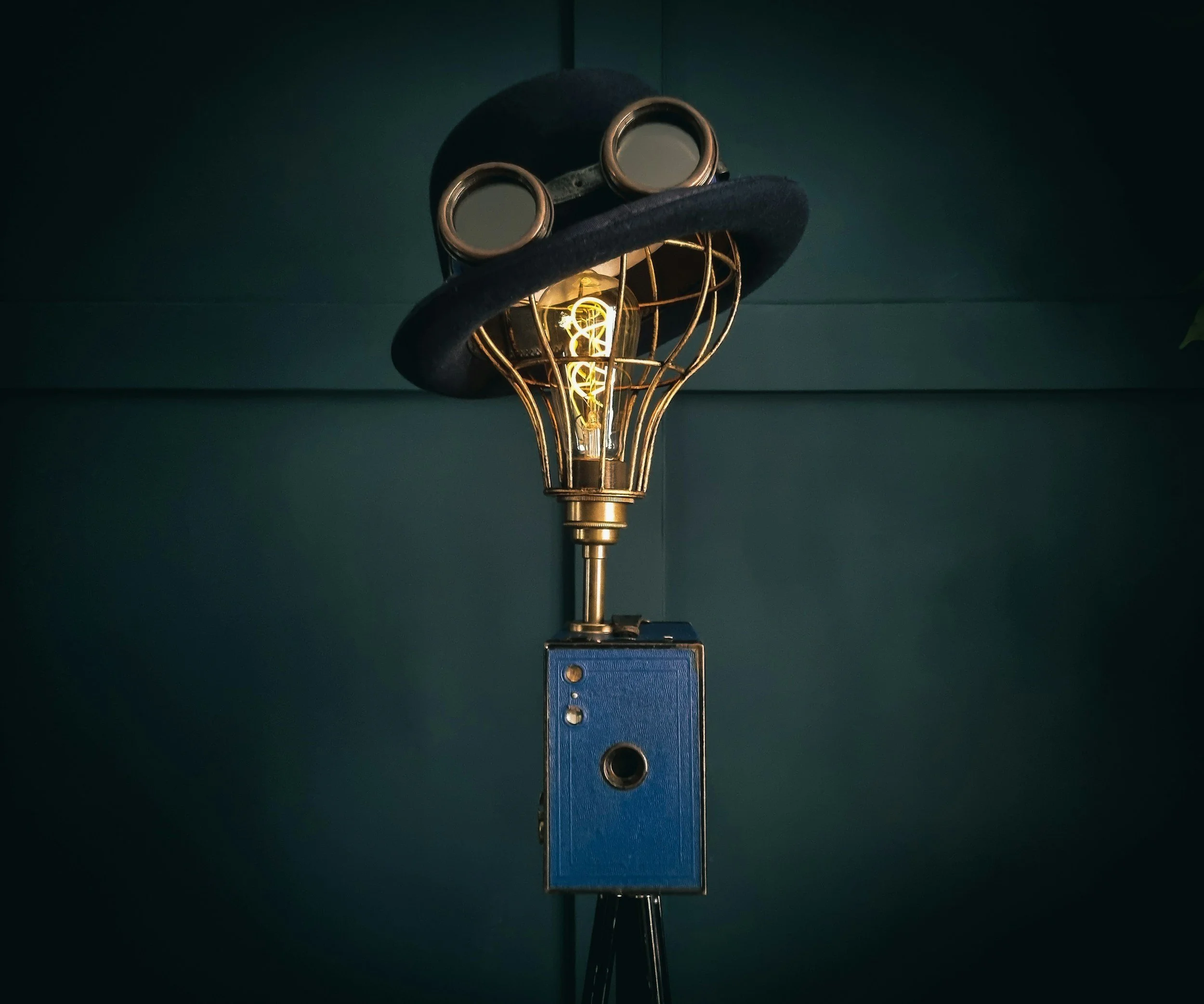 Une lampe à filament incandescent avec un support en métal, portée par une structure métallique bleue attachée à un mur vert foncé