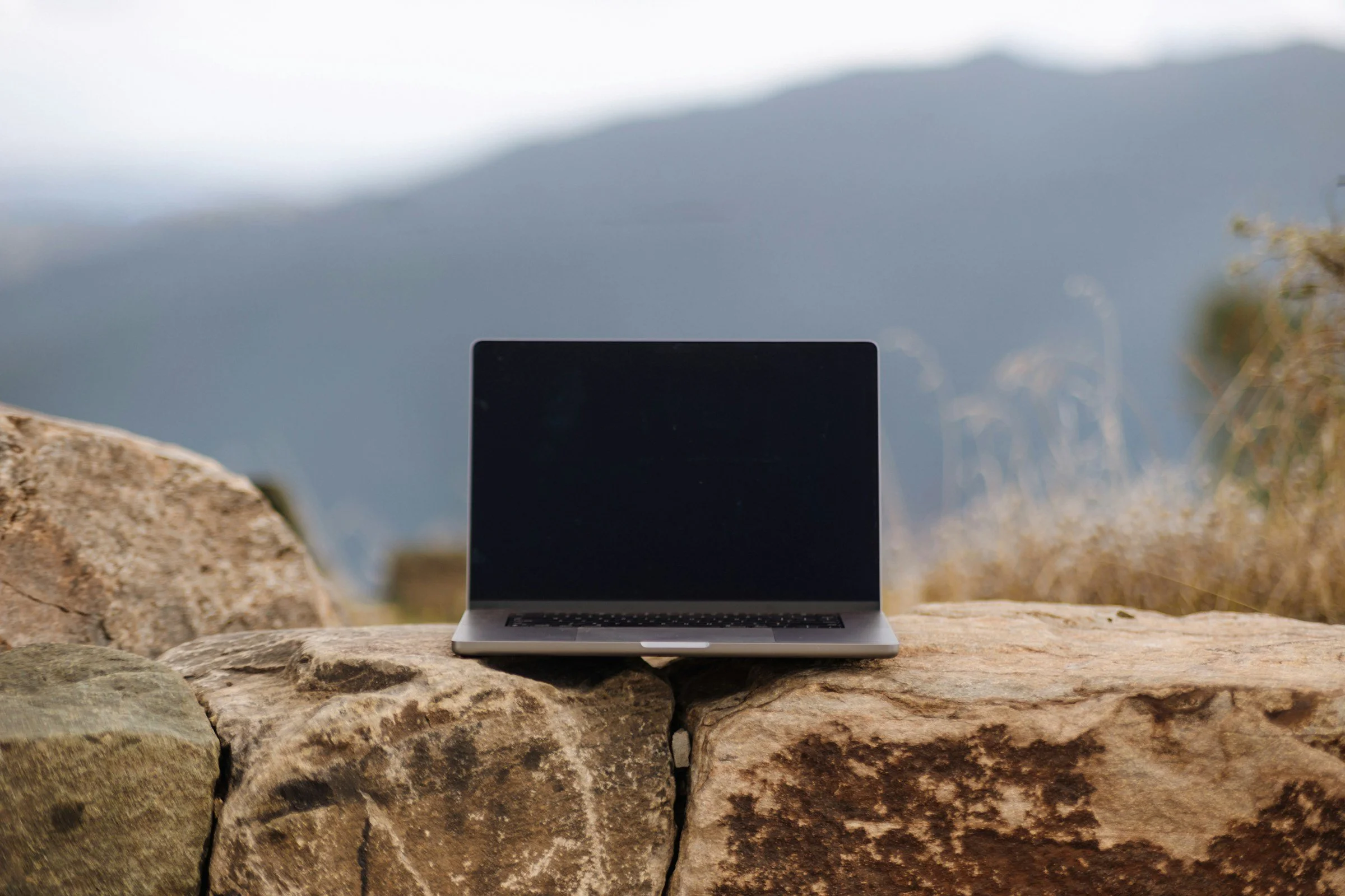 A laptop placed on a large, textured rock outdoors with a blurred mountain landscape in the background.