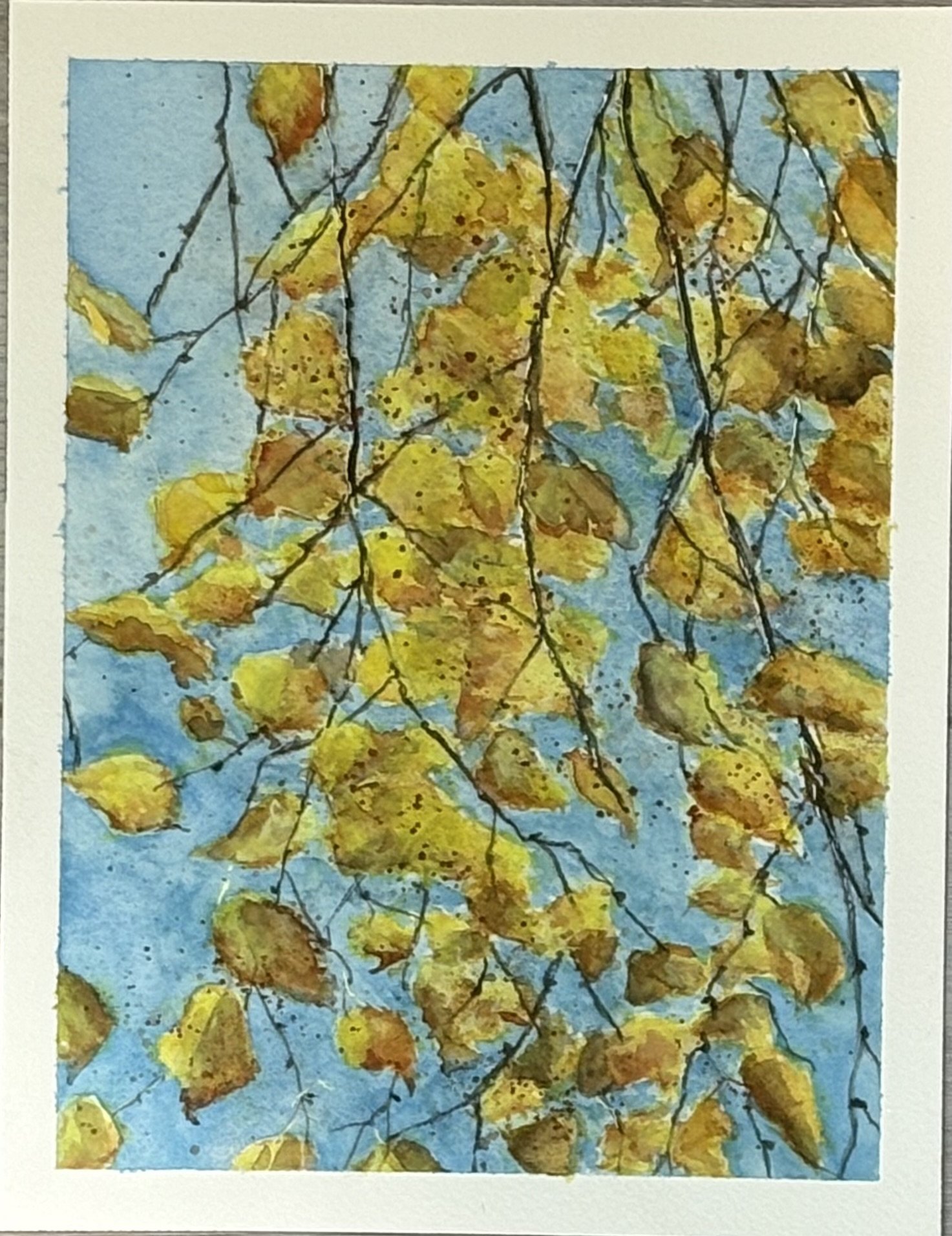 Watercolor painting of autumn tree branches with yellow and brown leaves against a blue sky background. Autumn leaves coming off of tree branches in the journal painting.