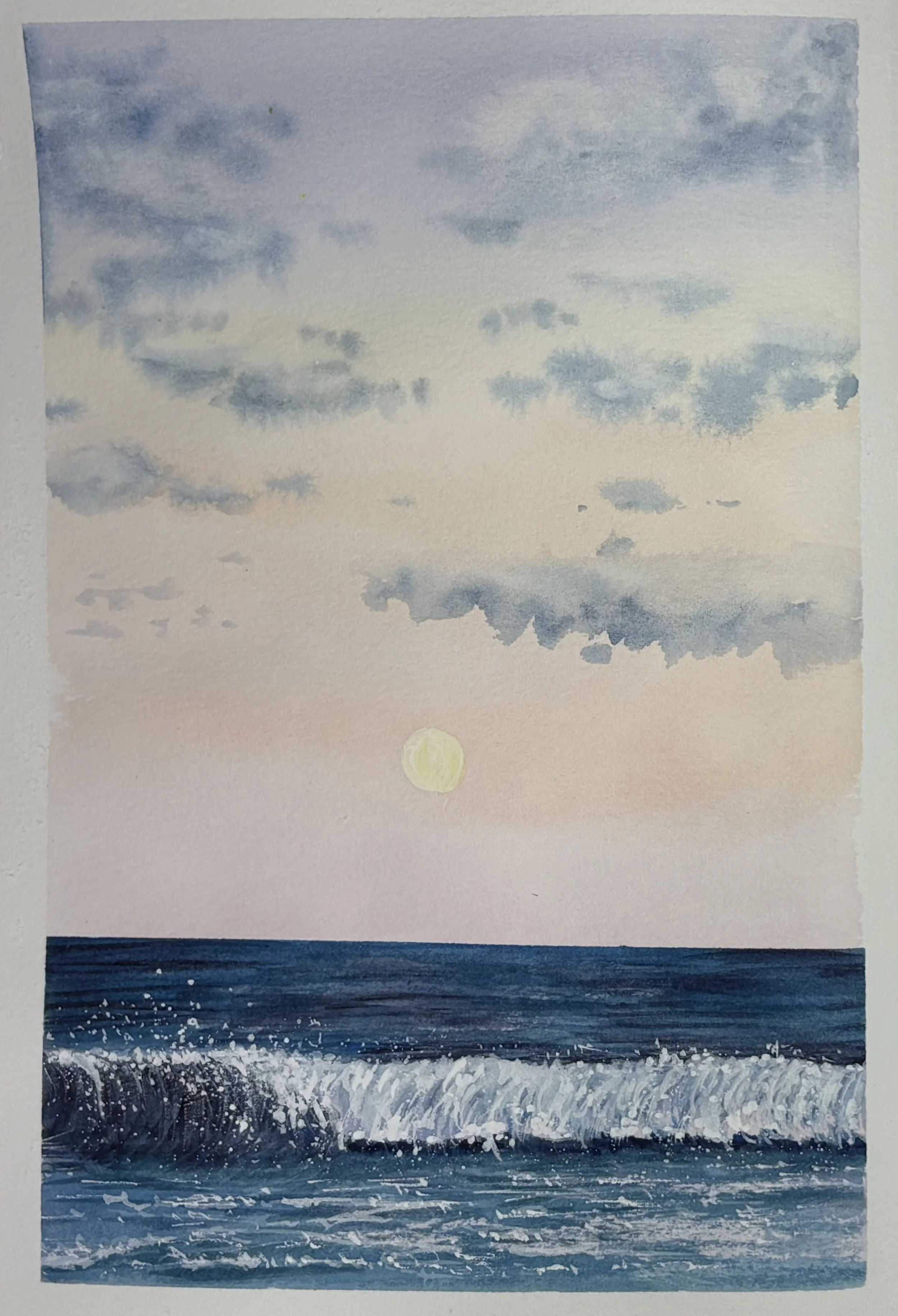 Watercolor painting of a beach scene at sunset with a full moon in the sky, clouds, ocean waves, and splashes of water. Journal painting of a wave with clouds on a beach.