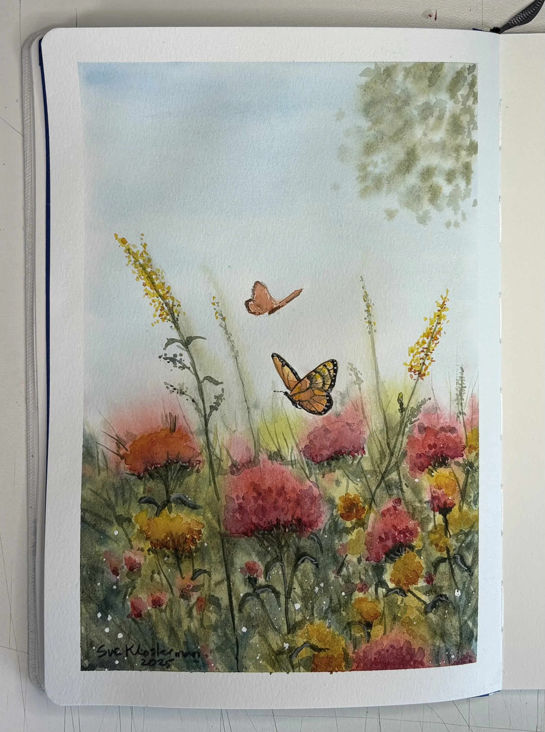 Watercolor painting of a garden scene with tall flowers in shades of yellow, orange, and pink, green stems and leaves, two butterflies with orange and black wings, a tree in the background with green foliage, and a light blue sky. Journal painting.
