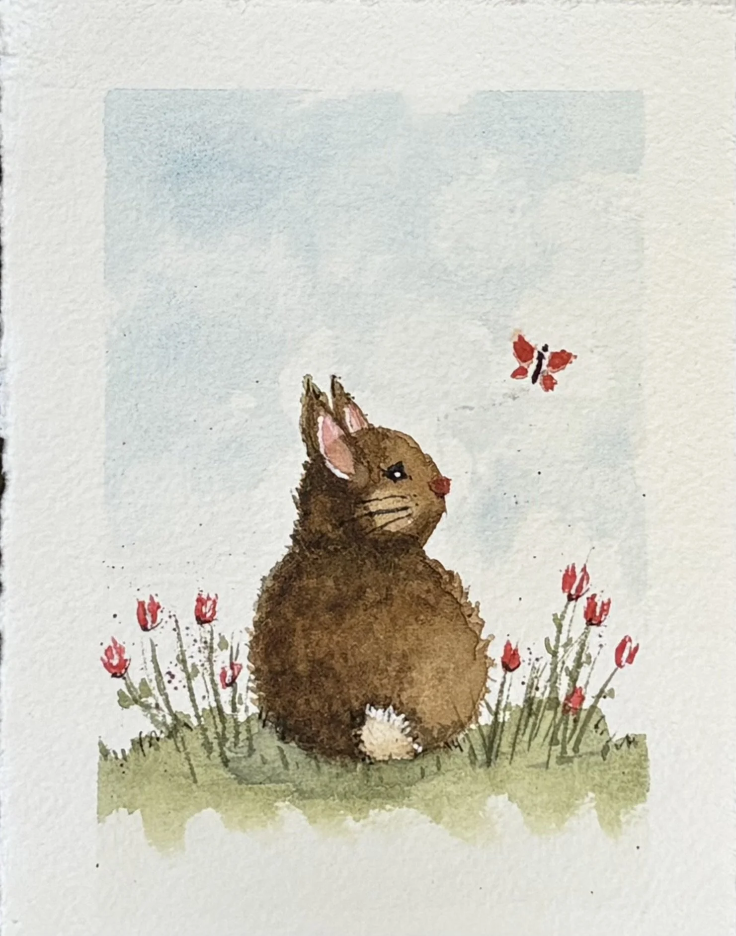 Watercolor illustration of a brown rabbit with pink ears sitting among small red flowers and a butterfly flying nearby. This is watercolor practice painting in an Etchr journal.