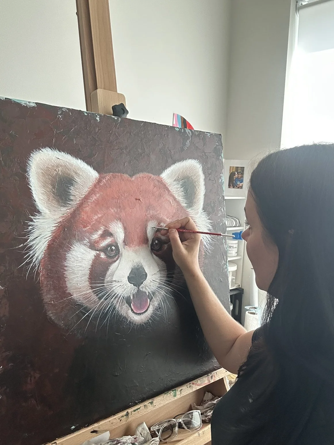 An artist painting a realistic portrait of a red panda on a canvas with acrylic paint.
