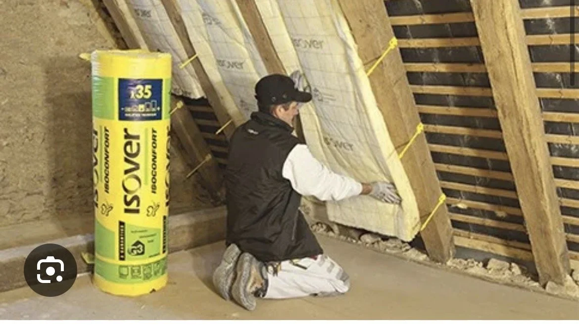 Persona instalando aislamiento en un techo de madera, con un rollo de aislamiento Isovent a su lado.