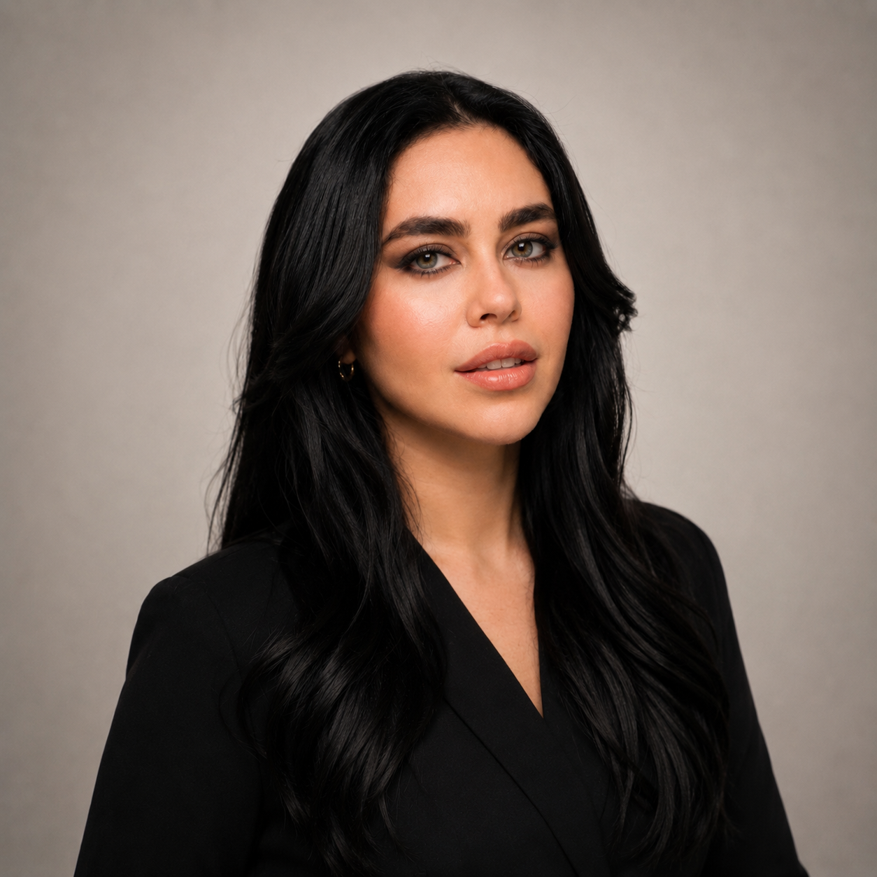 Mujer con cabello largo y ondulado, vestida con blazer negro, posando frente a fondo gris.