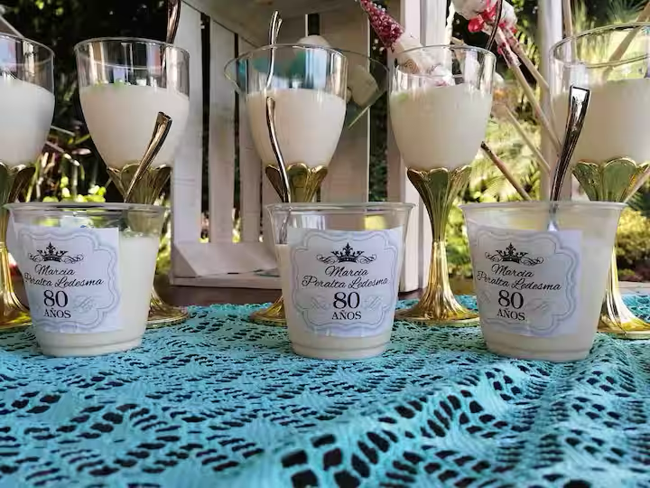 Celebration drinks with candles on a blue lace tablecloth, personalized for Marcia Prada Ledesma's 80th birthday.