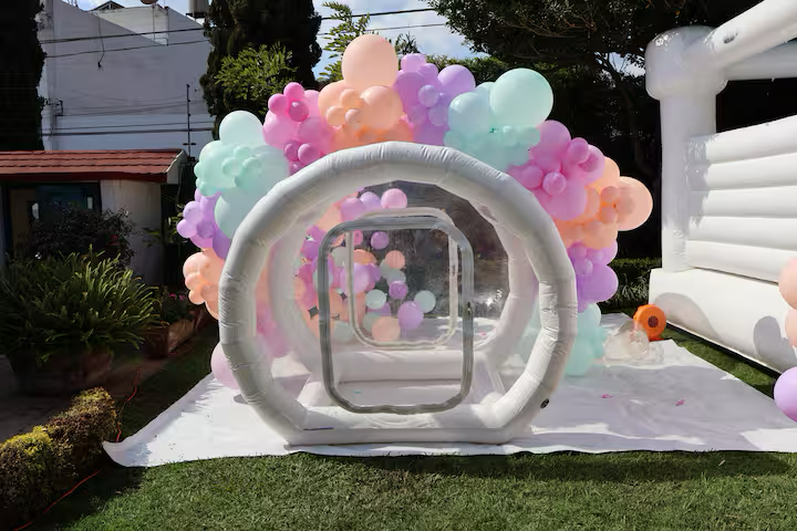 Inflatable bubble tent decorated with pastel-colored balloons for a celebration or event.
