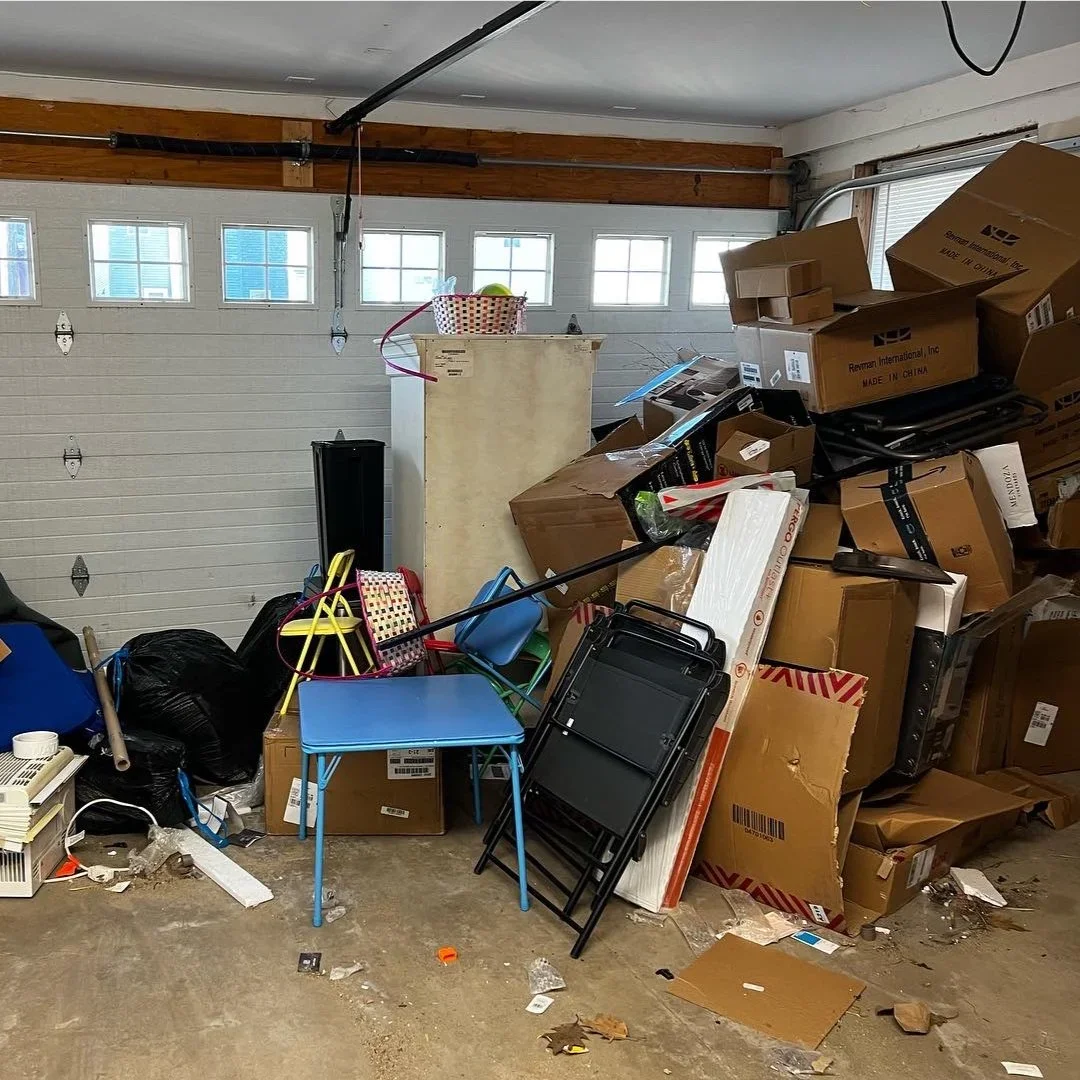 Cluttered garage with boxes, folding chairs, furniture, and miscellaneous household items before a garage cleanout.