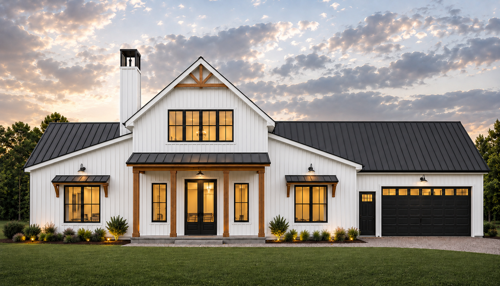 White modern farmhouse-style home with black roof, black window frames, and a black garage door, illuminated windows, surrounded by a manicured lawn and landscaping, during sunset with a cloudy sky.
