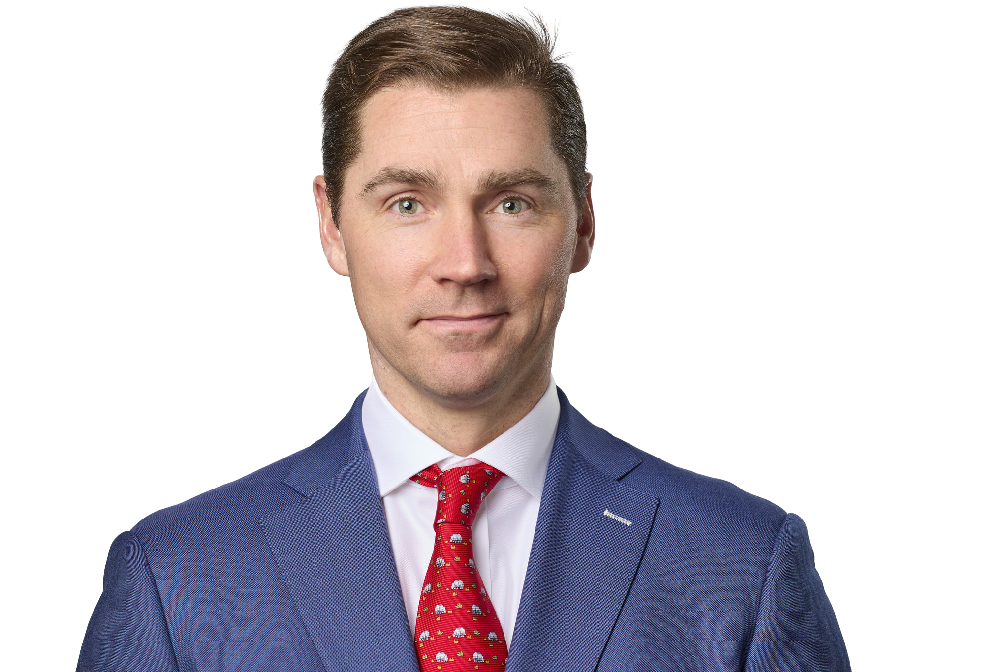 A man dressed in a blue suit with a white shirt and red tie featuring elephants, against a dark background.