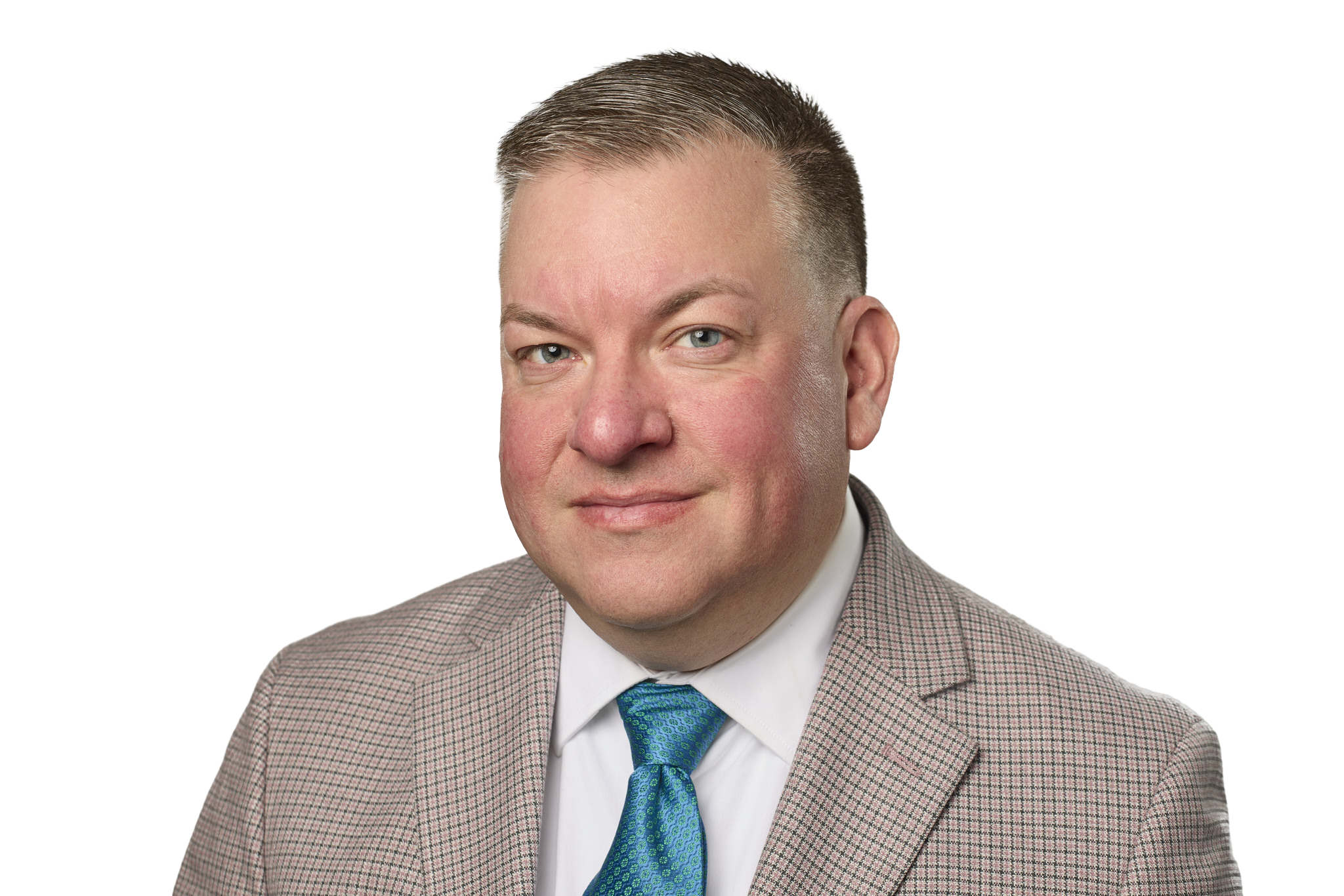 Close-up of a man in a checkered blazer, white shirt, and blue tie, smiling with short hair and light skin.