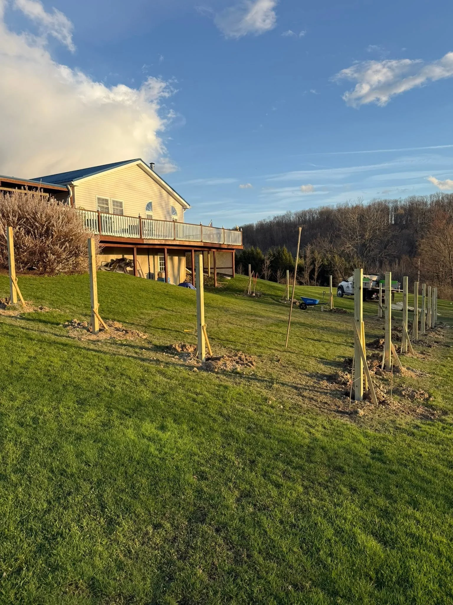 A house on a hill with a wooden balcony and a backyard being landscaped with new wooden posts and stakes.