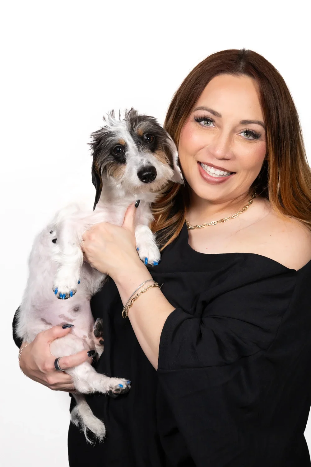 Smiling woman in a black top holds a small shaggy black-and-white dog against a white background.
