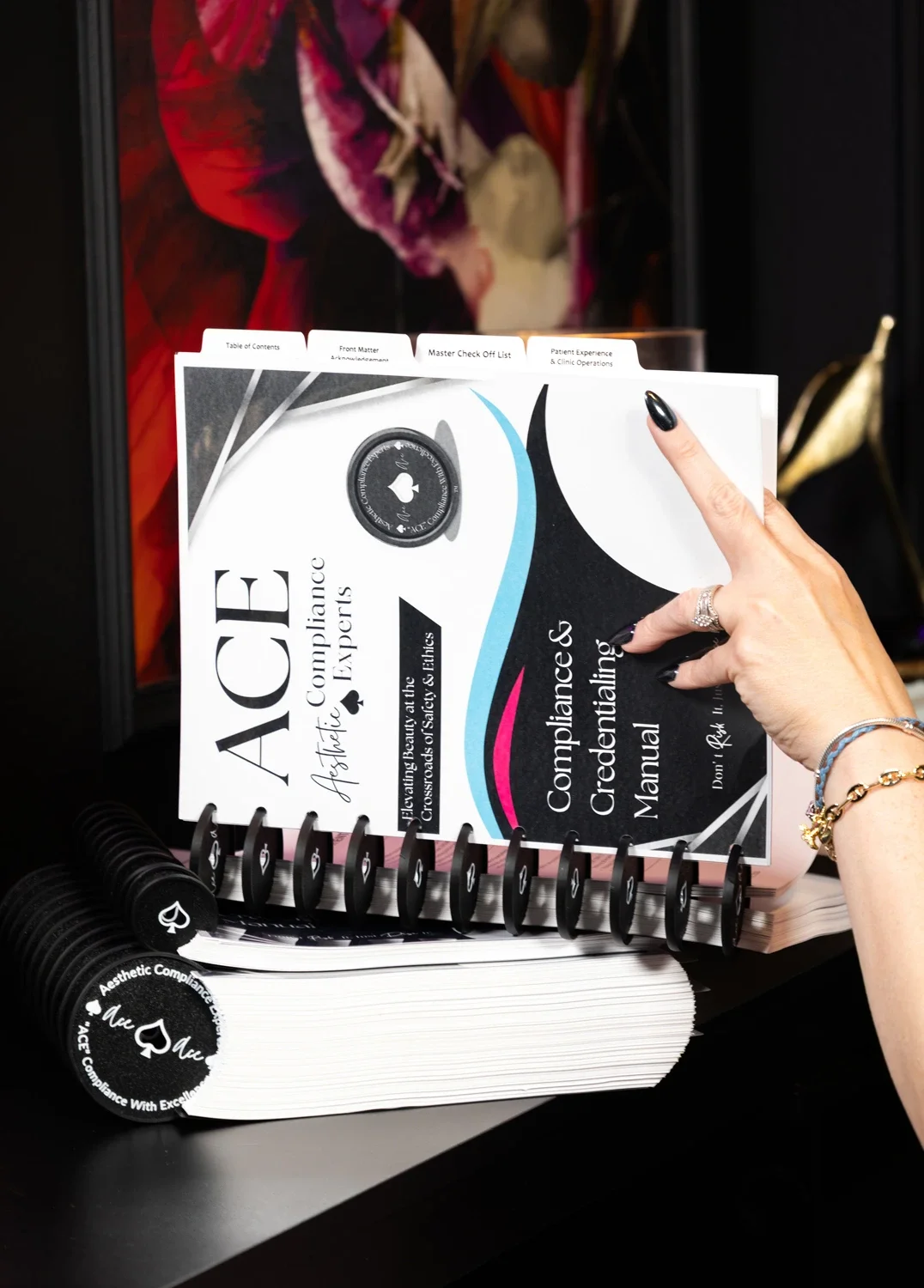 Open ACE Compliance & Credibility Manual held open stacked above two other disc-bound manuals.