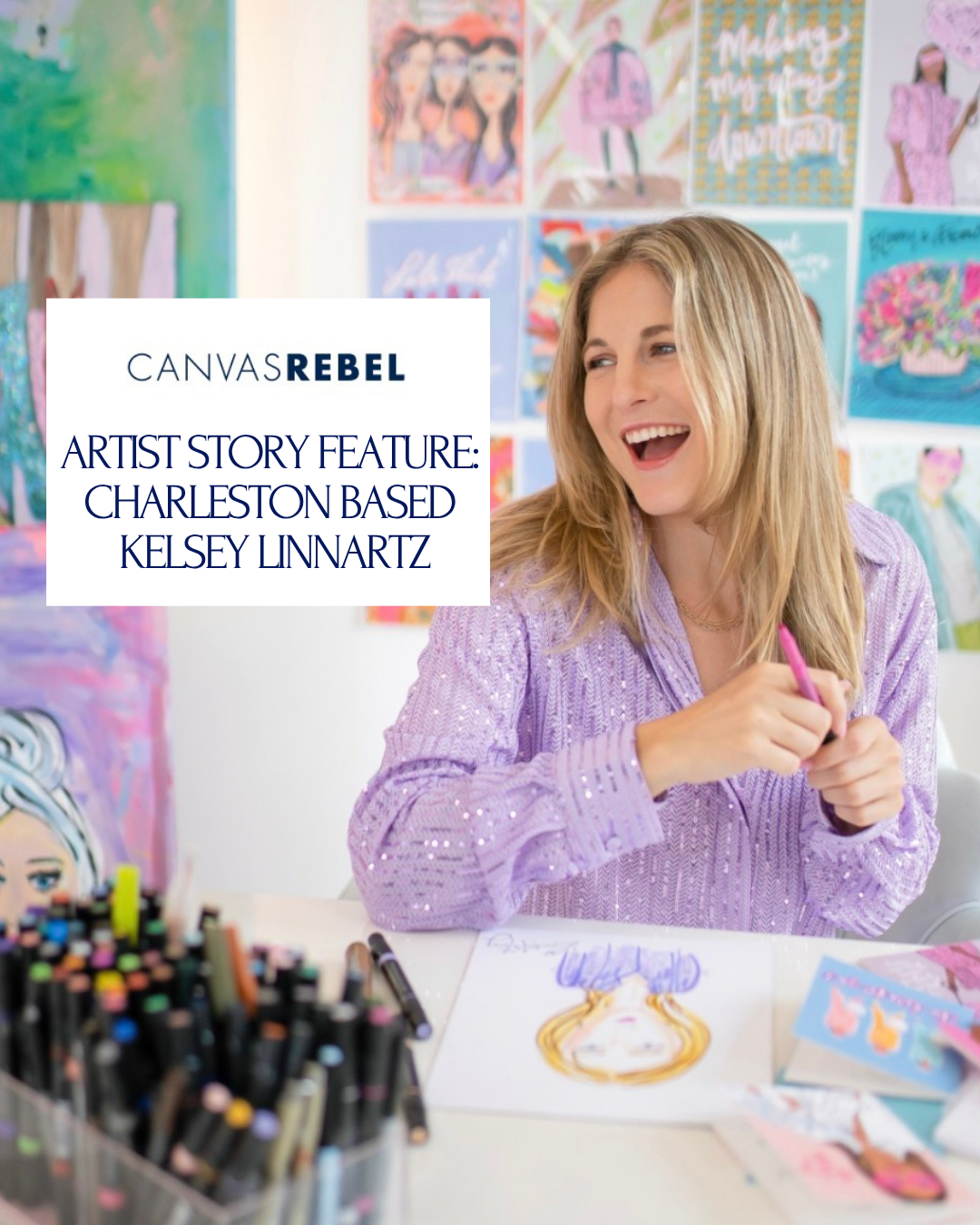A woman with blonde hair wearing a purple sweater, smiling and holding a pink marker, sitting at a desk with colorful artwork on the walls behind her.