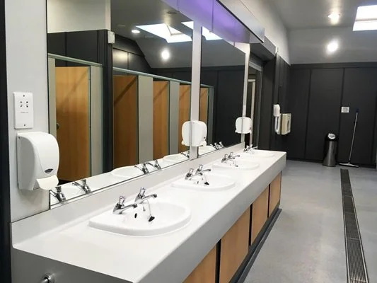 Public restroom with three sinks, mirrors, soap dispensers, and hand dryer, in a clean and modern setting.
