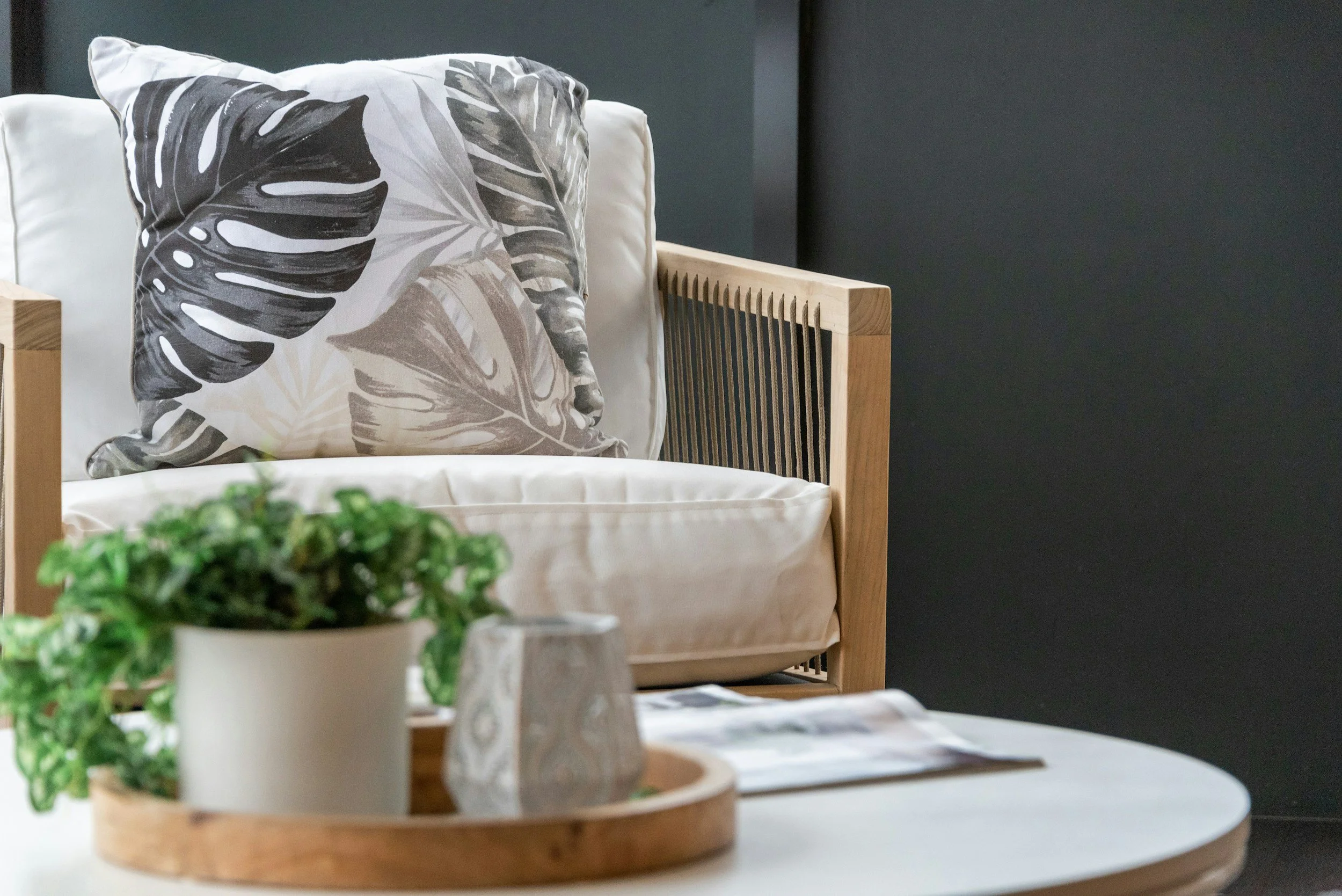 Close-up of a wooden-framed chair with a decorative pillow featuring a black and beige leaf pattern, set against a dark wall.