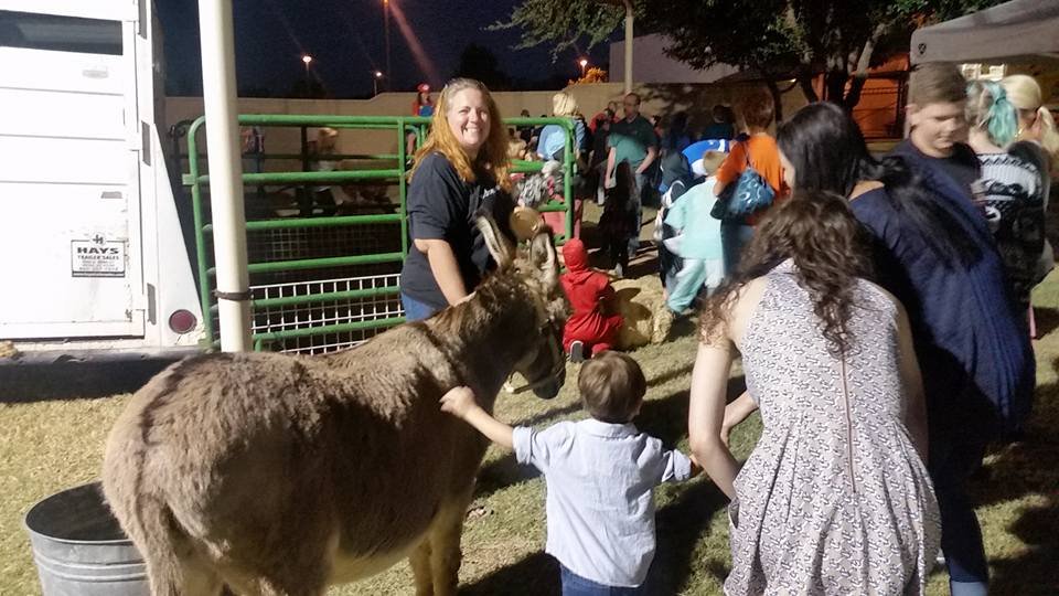 People visiting a petting zoo at night, feeding a small brown goat, with children and adults standing in line.
