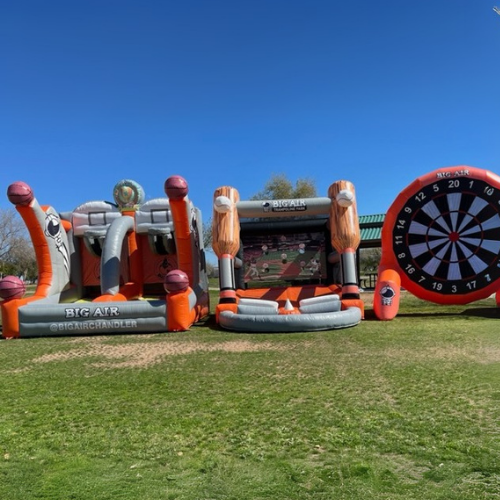 Sanborn Fall Festival in Chandler Outdoor inflatable play structure with a football-themed design, including a dartboard and a ladder, set up on a grassy field under a clear blue sky.