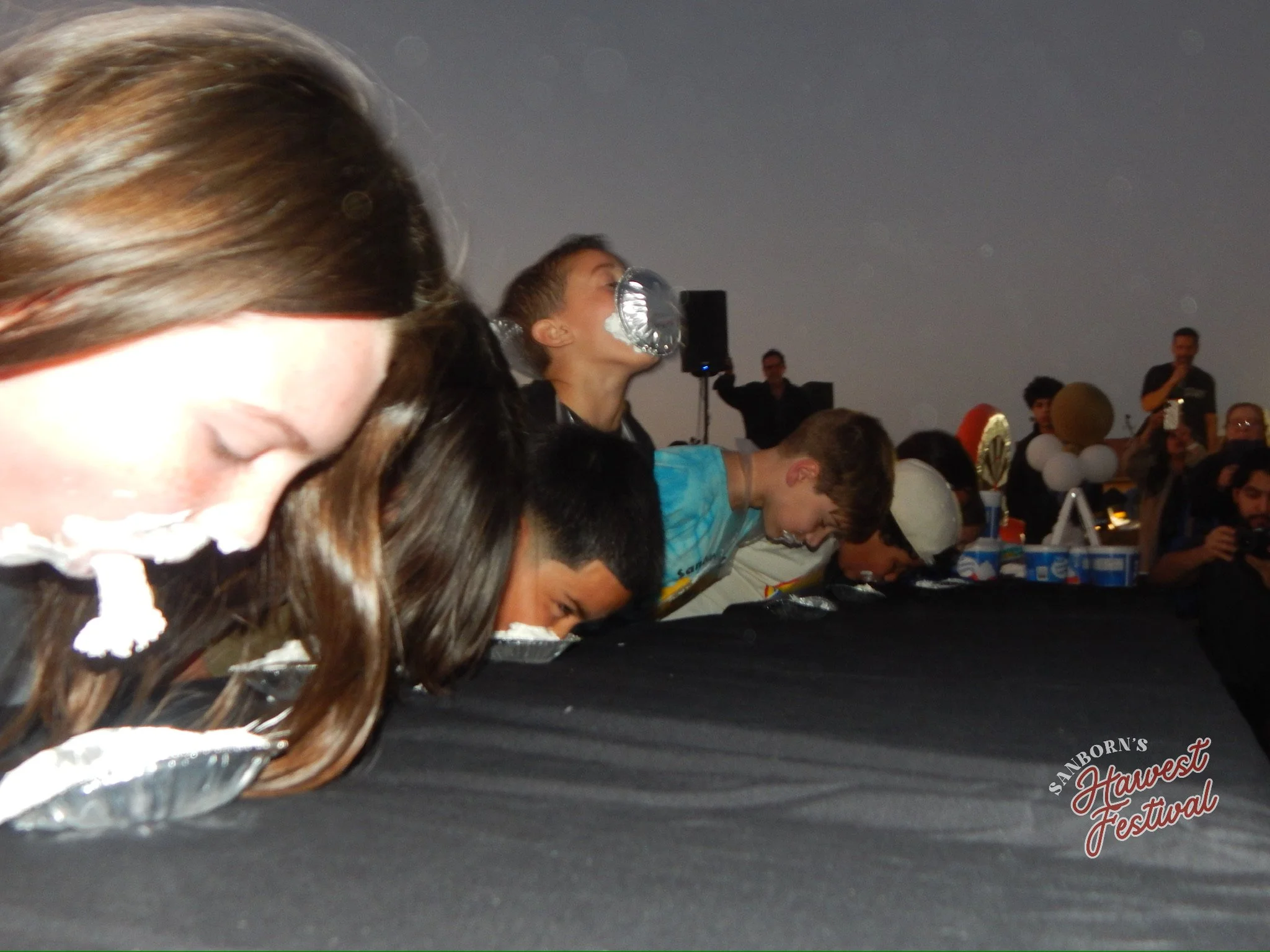 People sitting at a long table at the Sanborn's Harvest Festival, with a child holding a foil balloon.