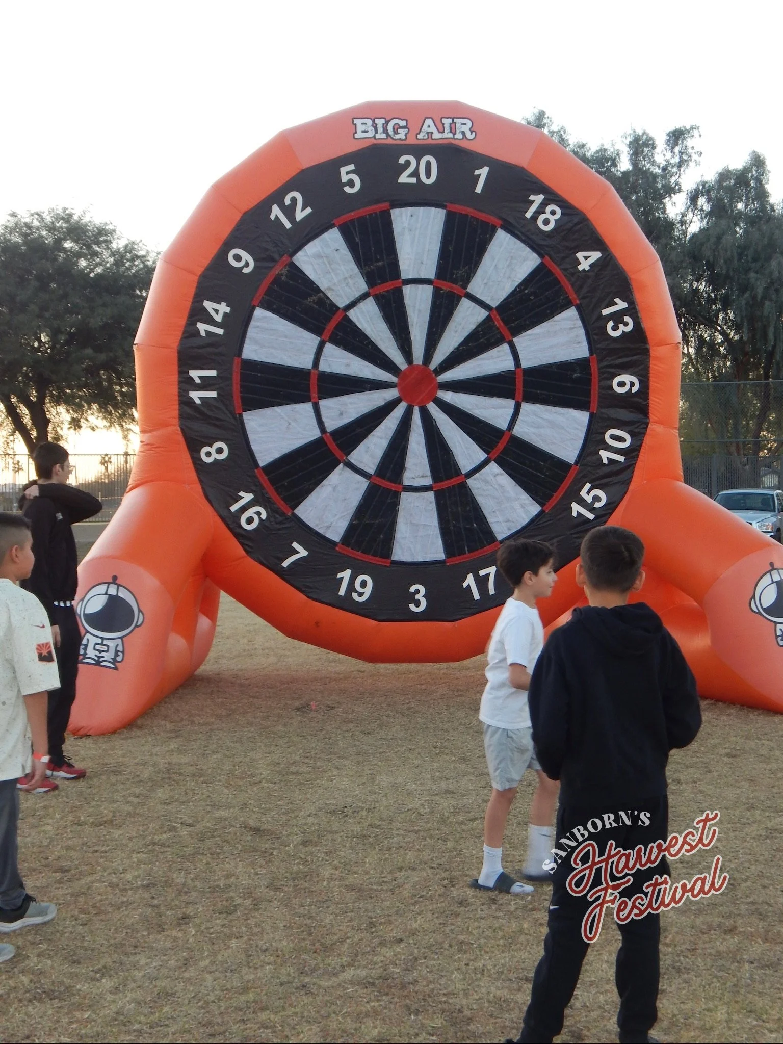 Children gathered around an inflatable mechanical dartboard at an outdoor festival during daytime.