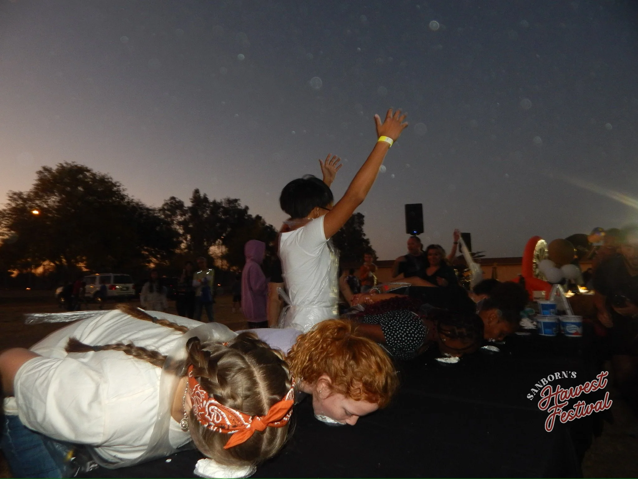 People bowing with their heads down at an outdoor event during the night, with fireworks visible in the sky.
