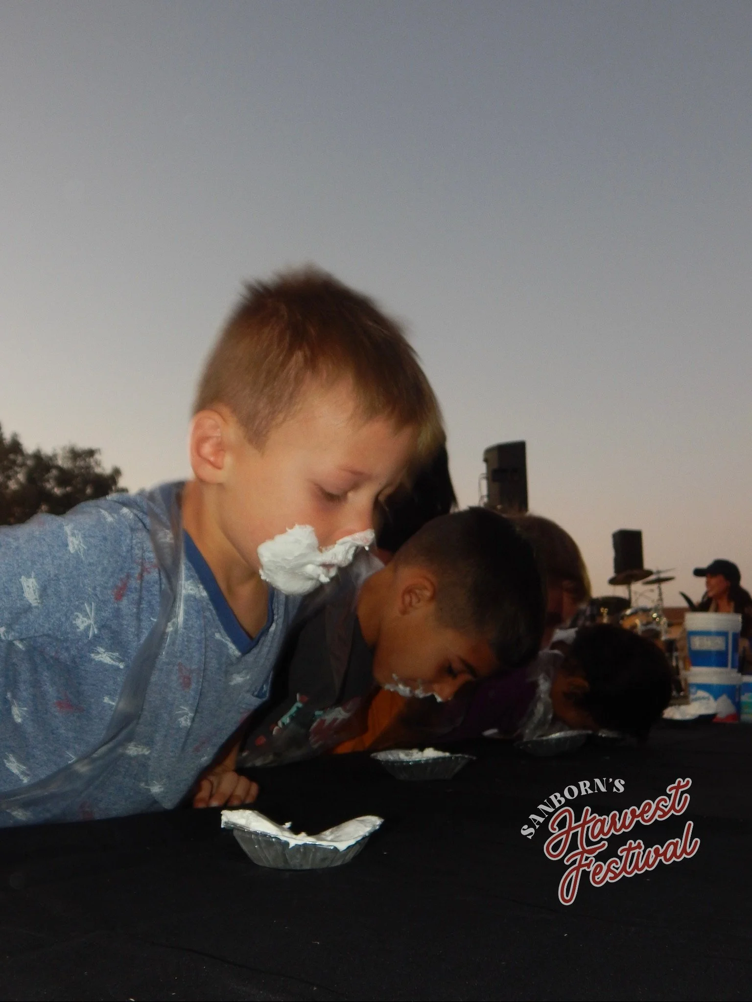 Children eating food at the Sanborn's Harvest Festival outdoor event during sunset.