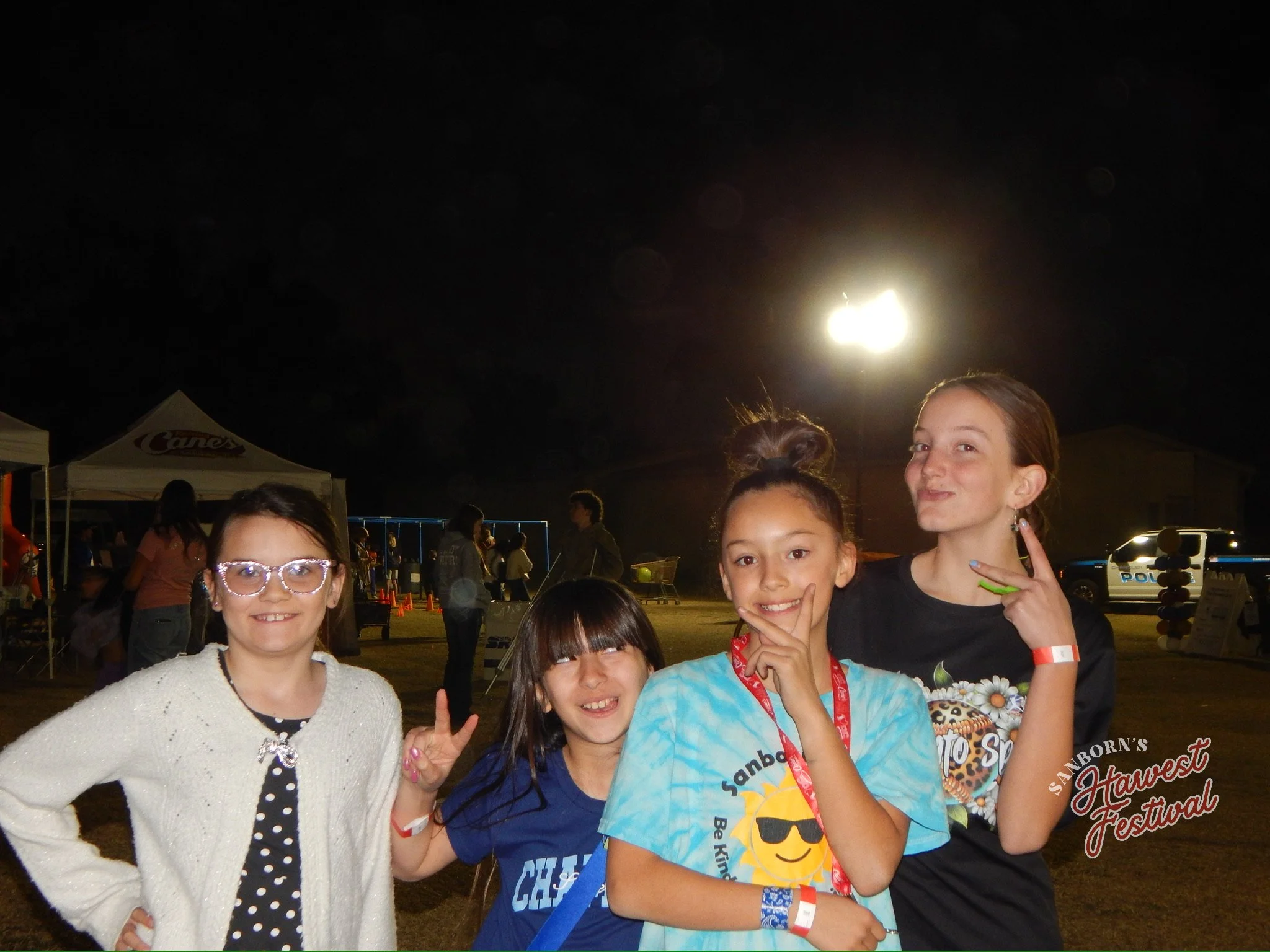 Group of smiling children at night, outdoors, at a festival or fair, with tents and a bright moon in the sky.
