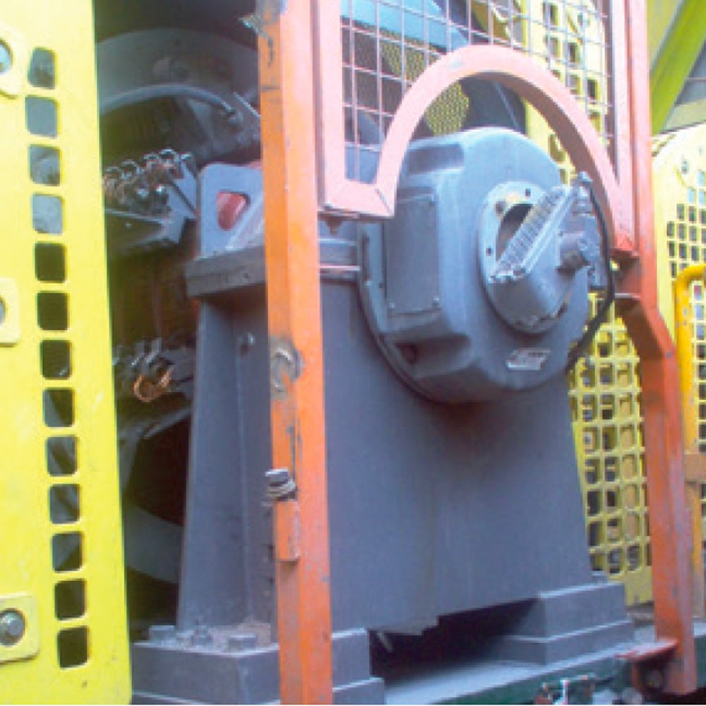 A large industrial machine with a black drum and motor, housed in a yellow and orange metal frame.