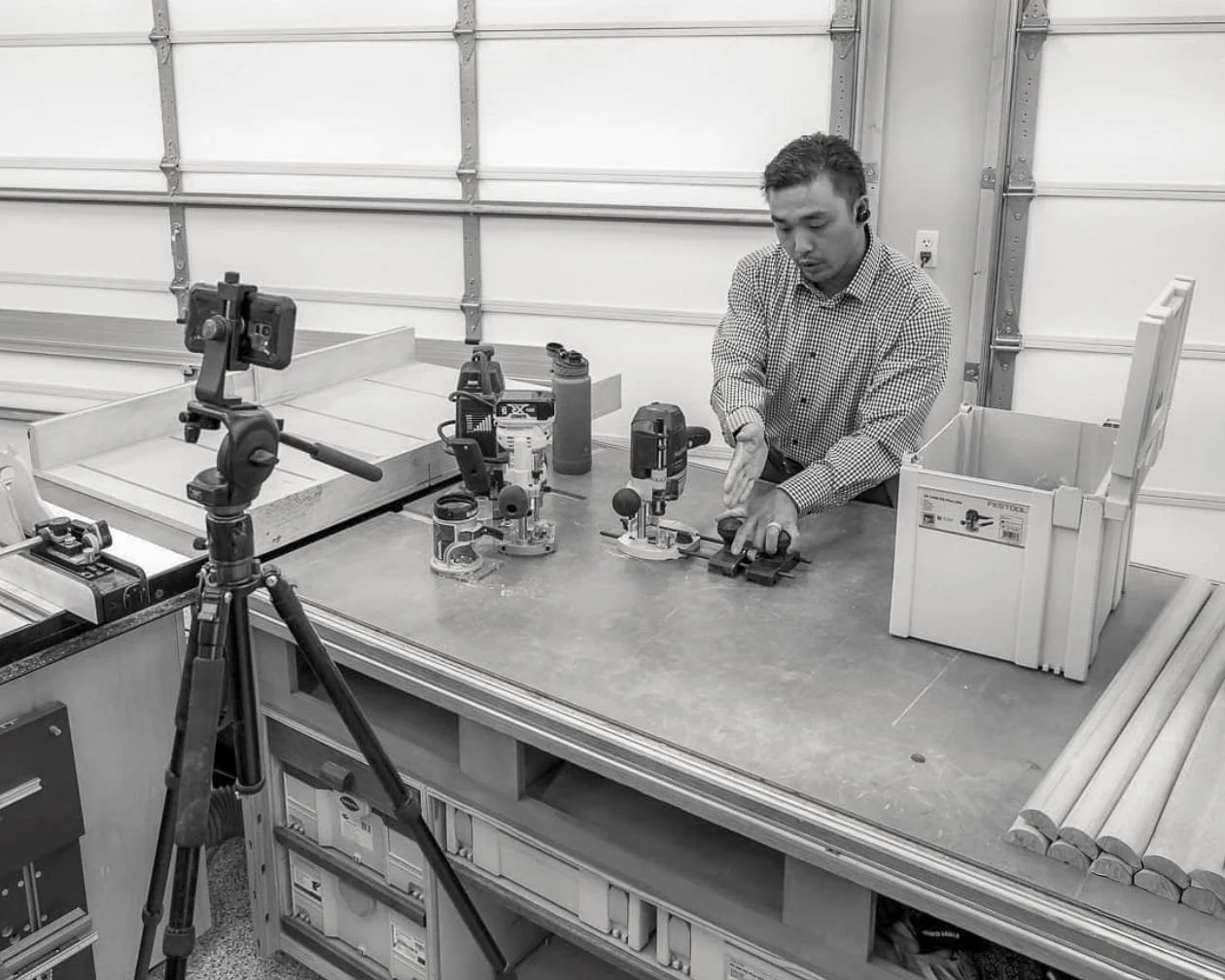 Huy demonstrating woodworking tools at a workbench while being recorded on camera.