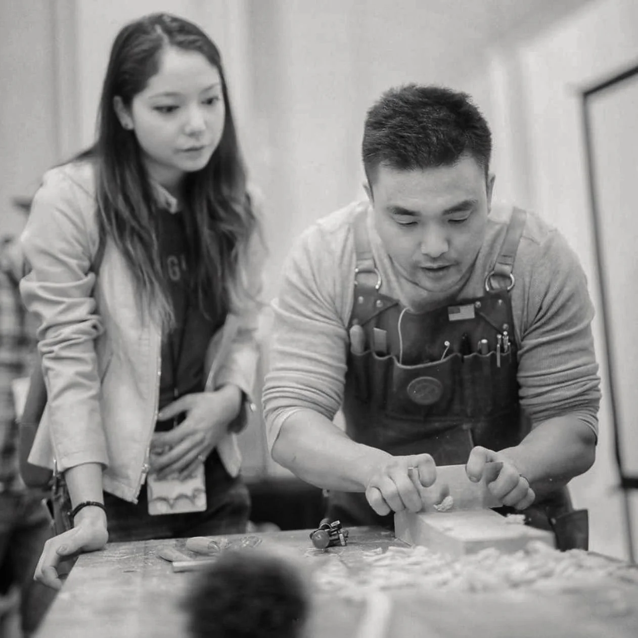 Woodworking instructor demonstrating hand-planing techniques with a workshop participant nearby.