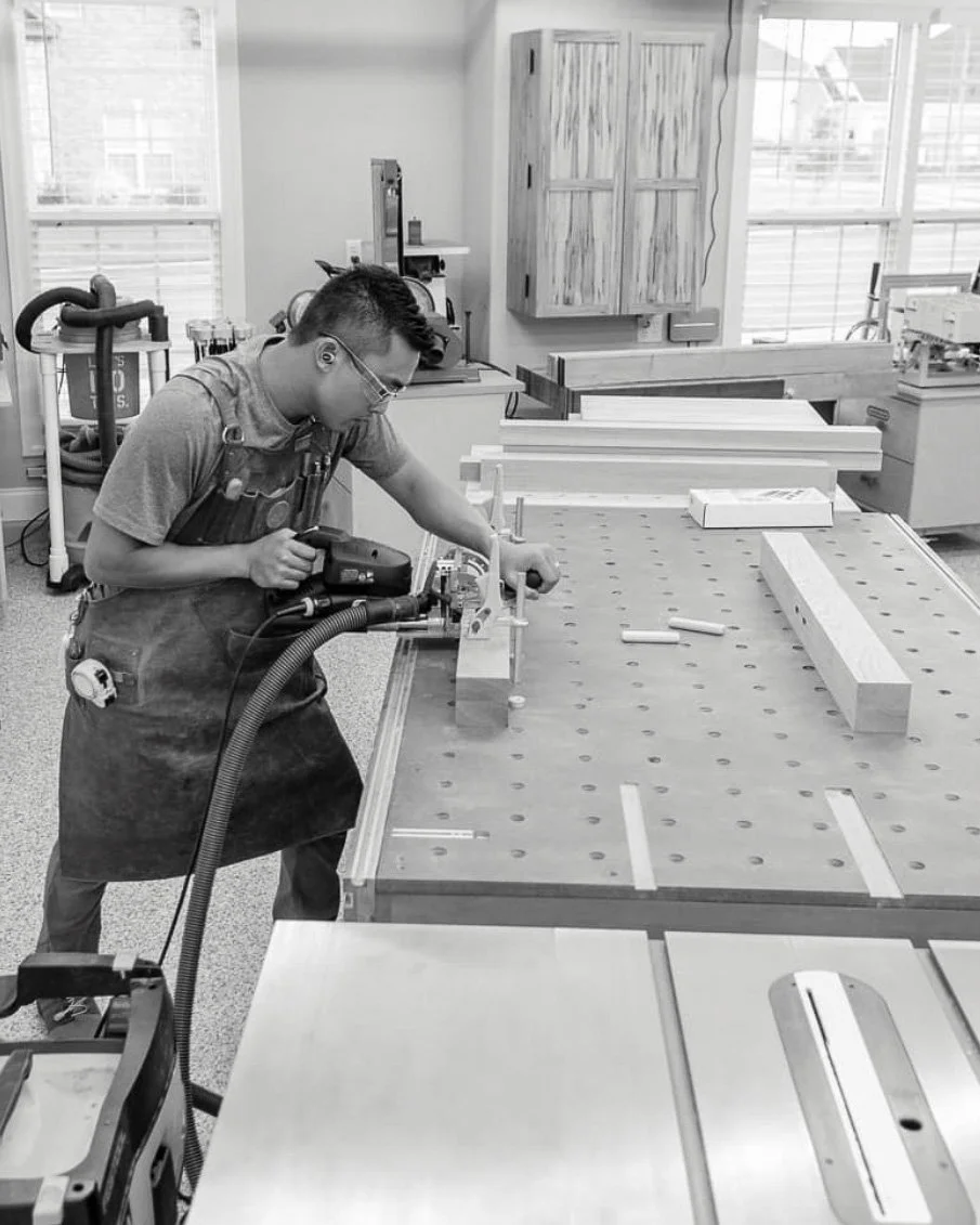 Huy Huynh working at a large workbench in his woodworking shop.