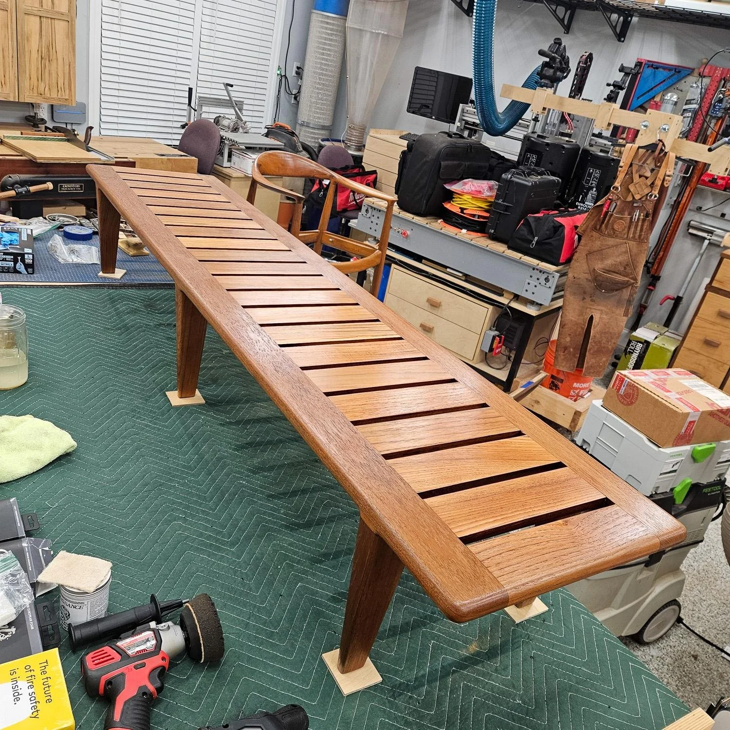 Hans J. Wegner JH 574 teak bench shown in the workshop during restoration, highlighting the long slatted frame and wood surface.