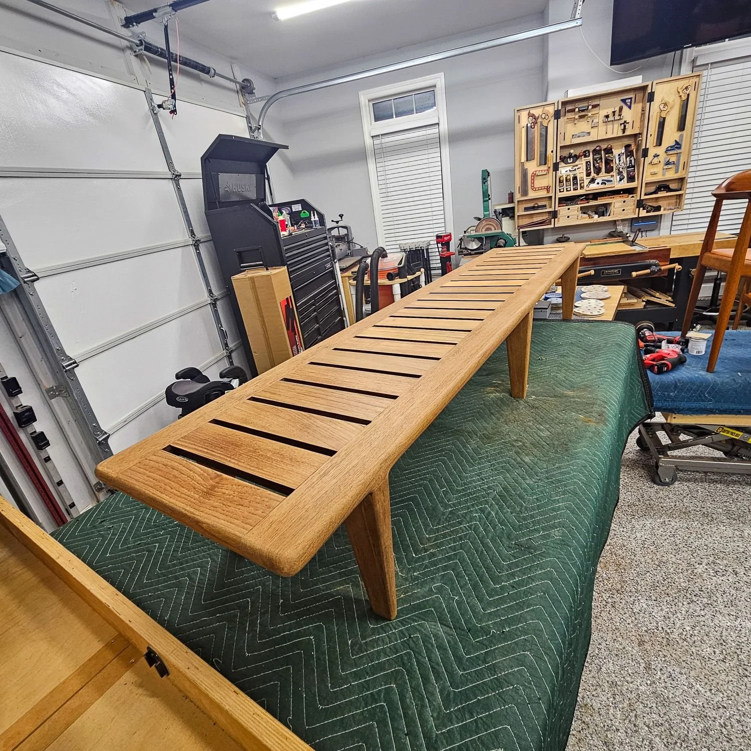 Hans J. Wegner JH 574 teak bench shown in the workshop during restoration, highlighting the long slatted frame and restored wood.