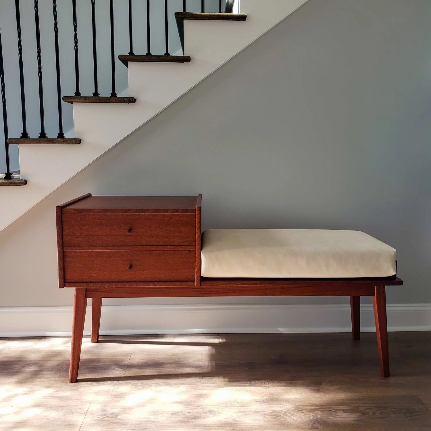 Straight-on view of the handmade walnut Gossip Bench in a residential interior, showing the upholstered seat and built-in drawers.