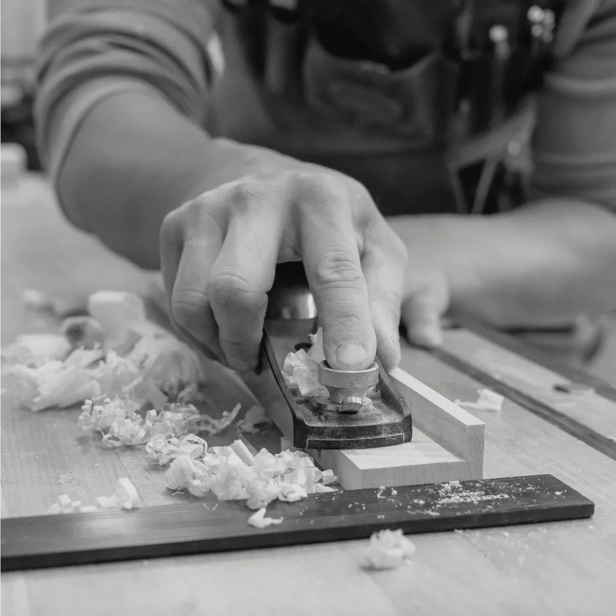 Huy using a hand plane to smooth a piece of wood in a woodworking workshop, with wood shavings on the work surface.