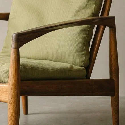 Close-up of the sculpted rosewood arm and frame on a Kai Kristiansen Model 121 Paper Knife chair with temporary green upholstery.