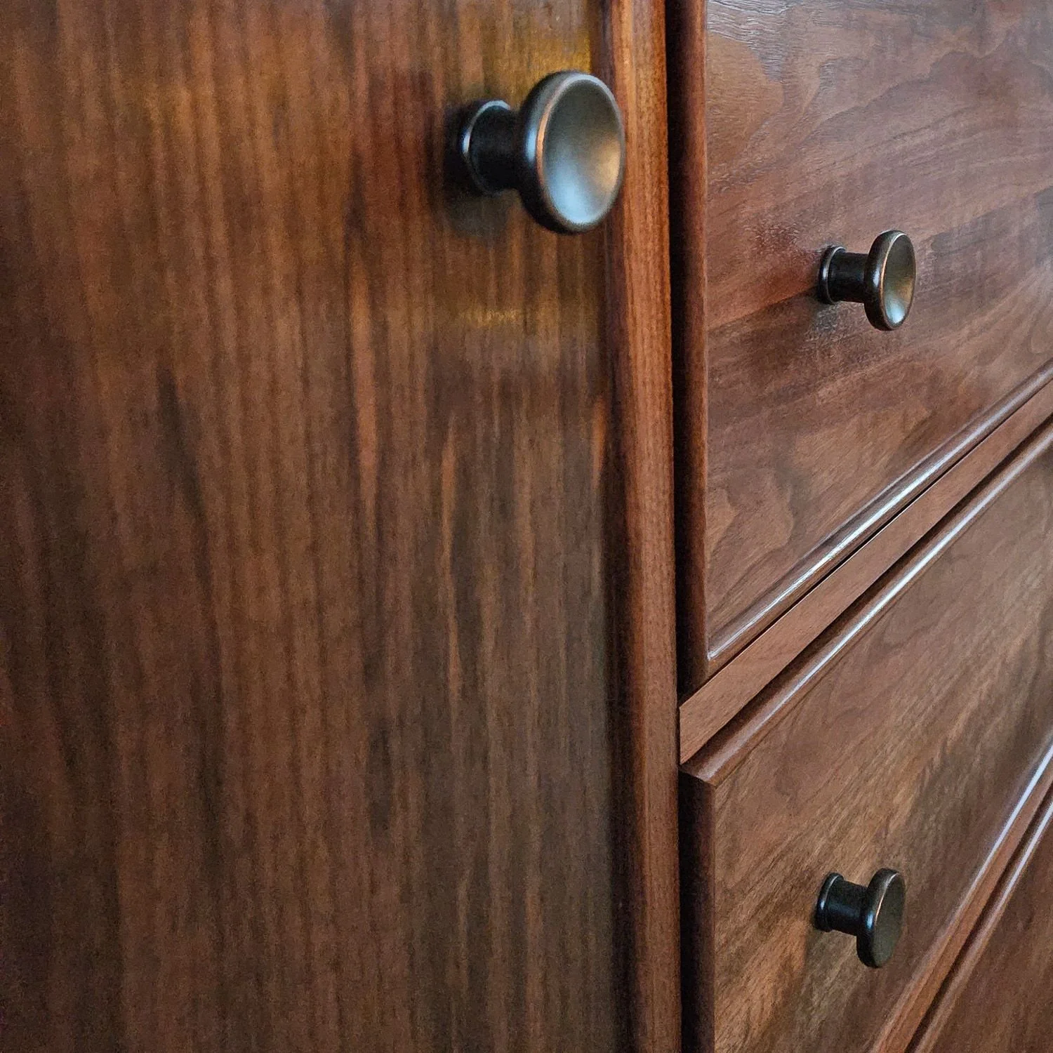 Close-up of the walnut sideboard showing the dark metal knobs, drawer fronts, door panel, and wood grain.