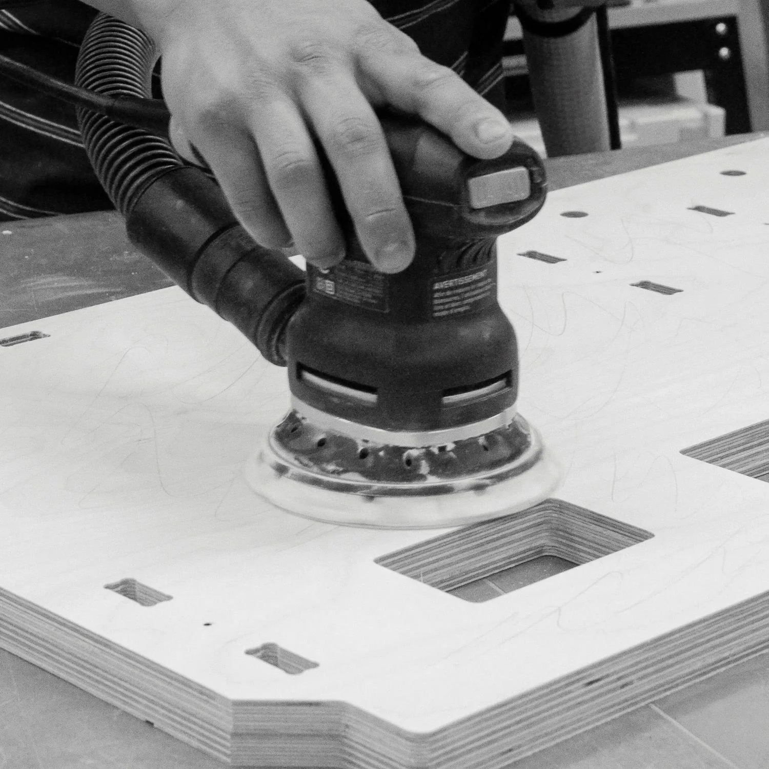 Close-up of a random orbital sander being used on a plywood panel in the workshop.