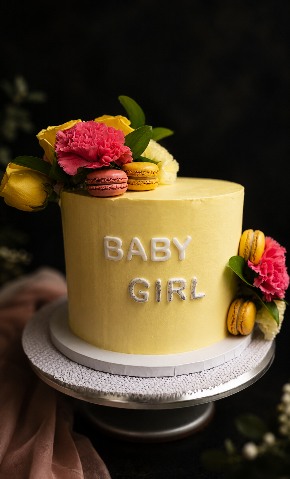 Yellow Baby Girl celebration cake decorated with pink and yellow flowers and macarons.